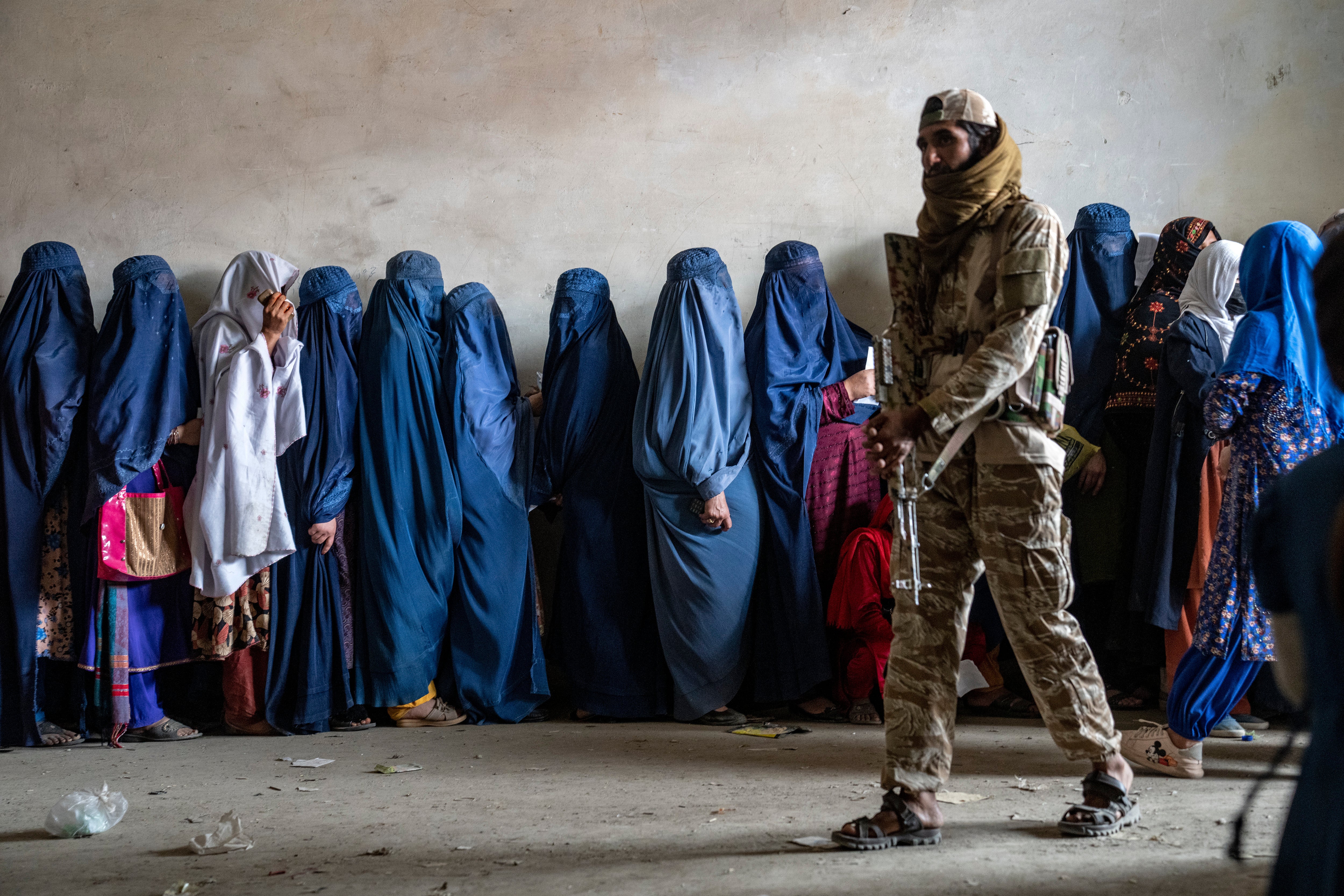 Hundreds of Afghan women and girls, seen here queuing for food under Taliban guard, are among those stranded abroad waiting for UK visas