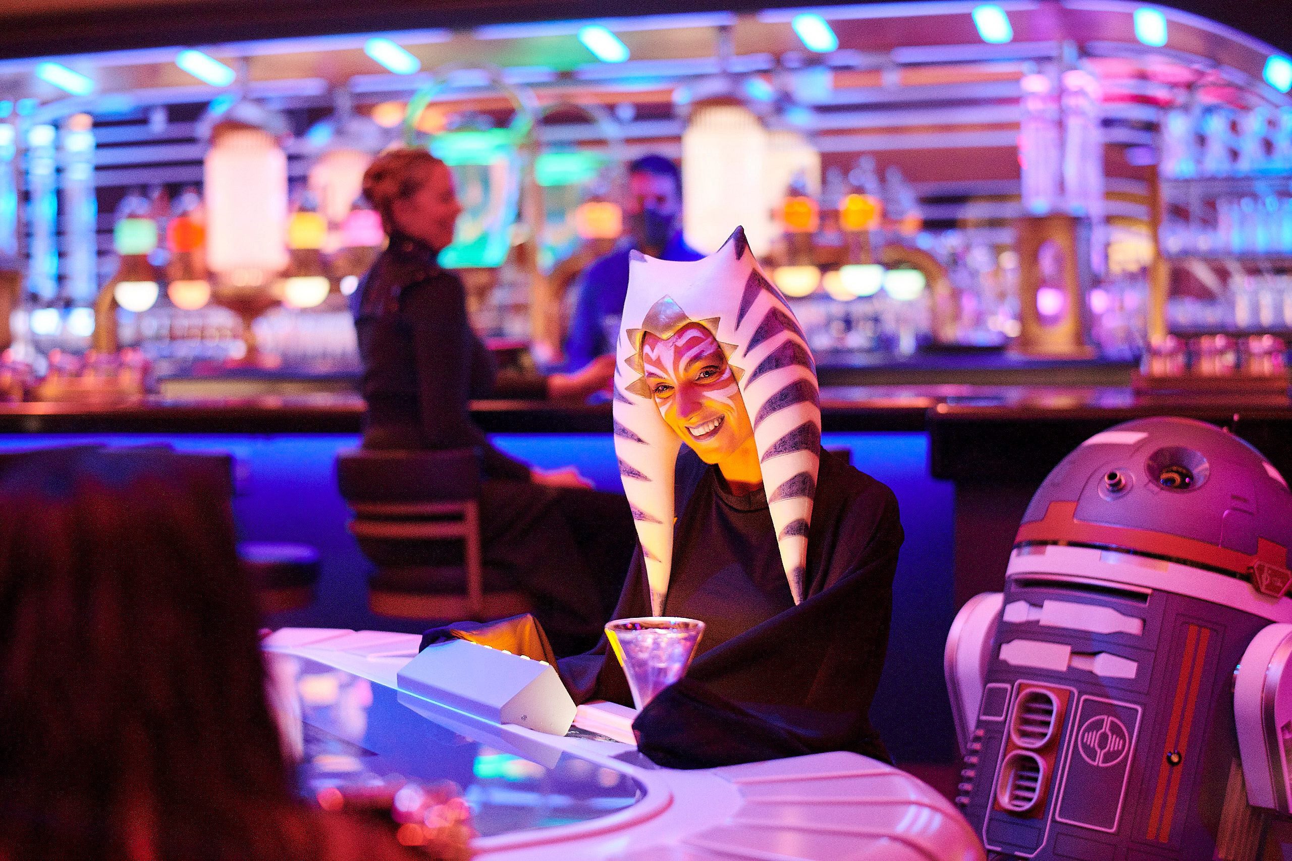 A passenger wearing a Togruta headpiece sits at the holo-sabacc table in the Star Wars: Galactic Starcruiser