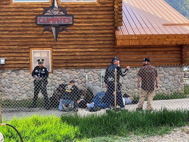 Un oficial de policía hace guardia mientras un hombre con un parche Bandidos MC ayuda a un motociclista baleado en Red River, Nuevo México, después de un tiroteo entre miembros de dos pandillas de motociclistas en un mitin anual de motos del Día de los Caídos.