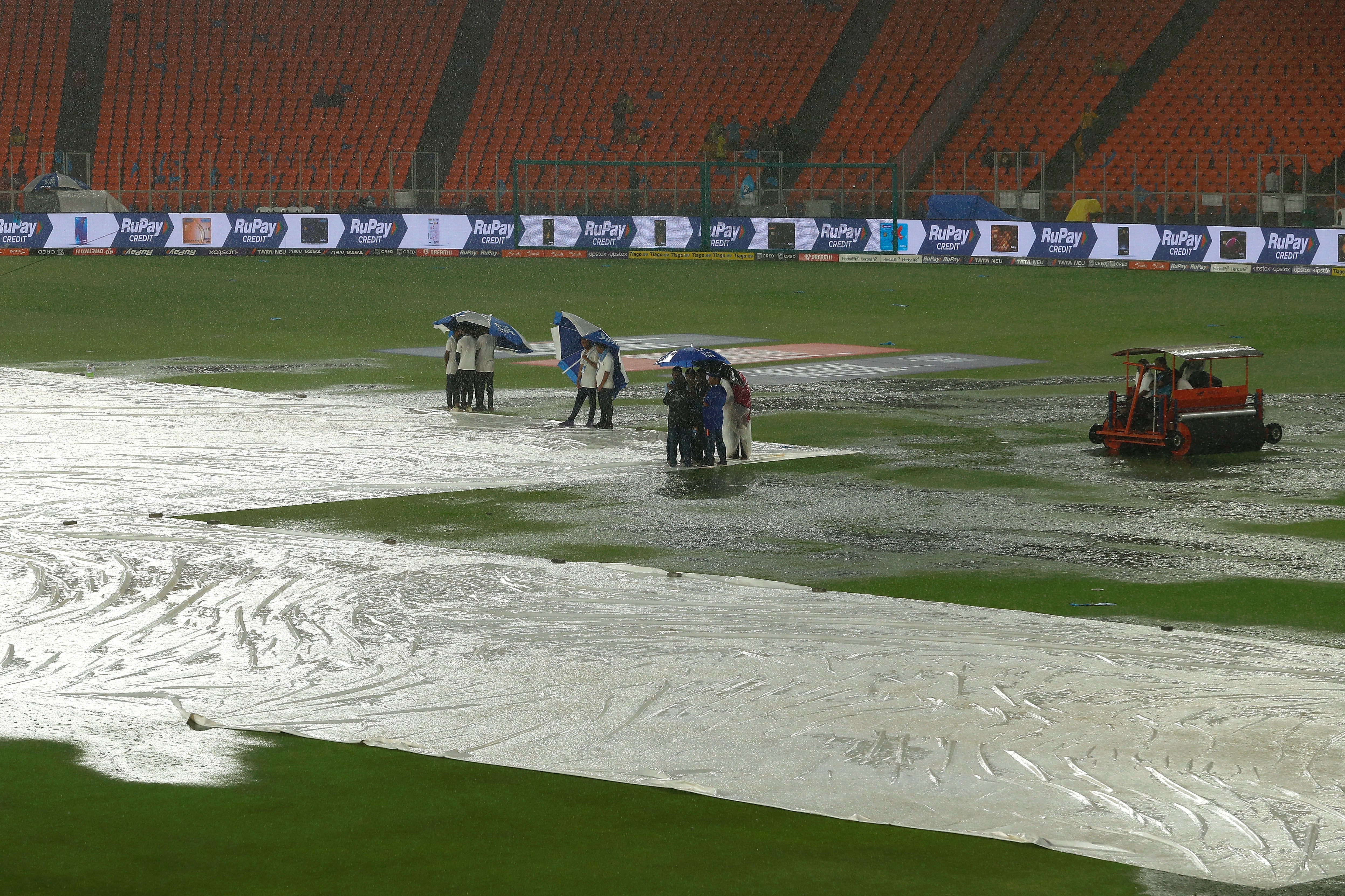 Ground staff huddle under umbrellas as rain delays the start of play during the 2023 IPL Final match between Chennai Super Kings and Gujarat Titans at Narendra Modi Stadium on 28 May 2023 in Ahmedabad