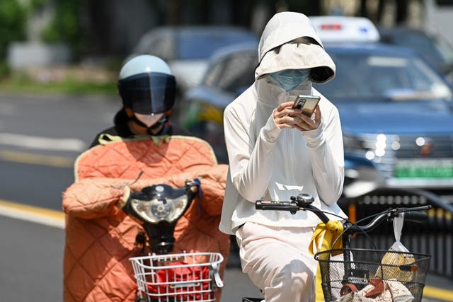 <p>A woman wearing sun protective clothing commutes on a bicycle amid hot weather in Shanghai on Monday </p>