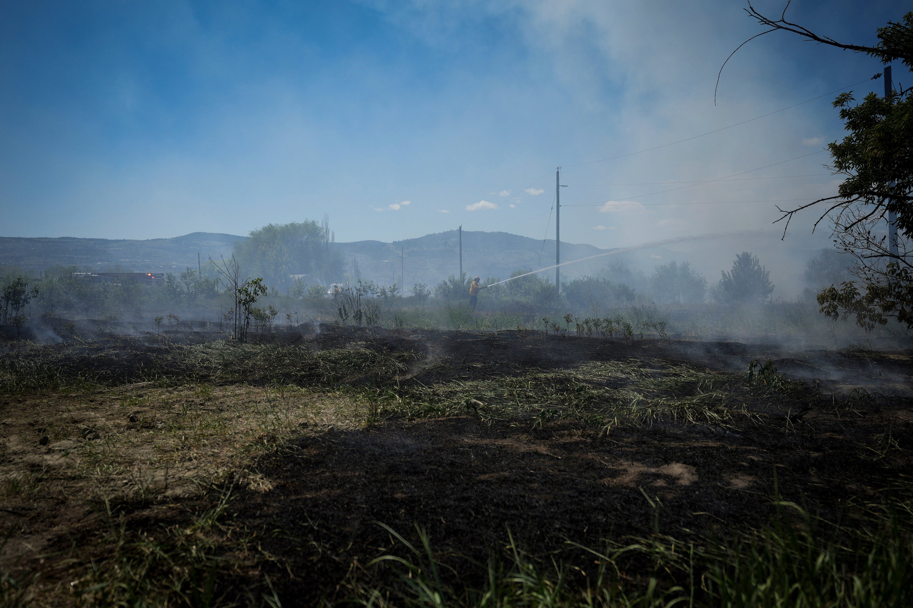 A firefighter directs water on a grass fire on an acreage behind a residential property in Kamloops, British Columbia
