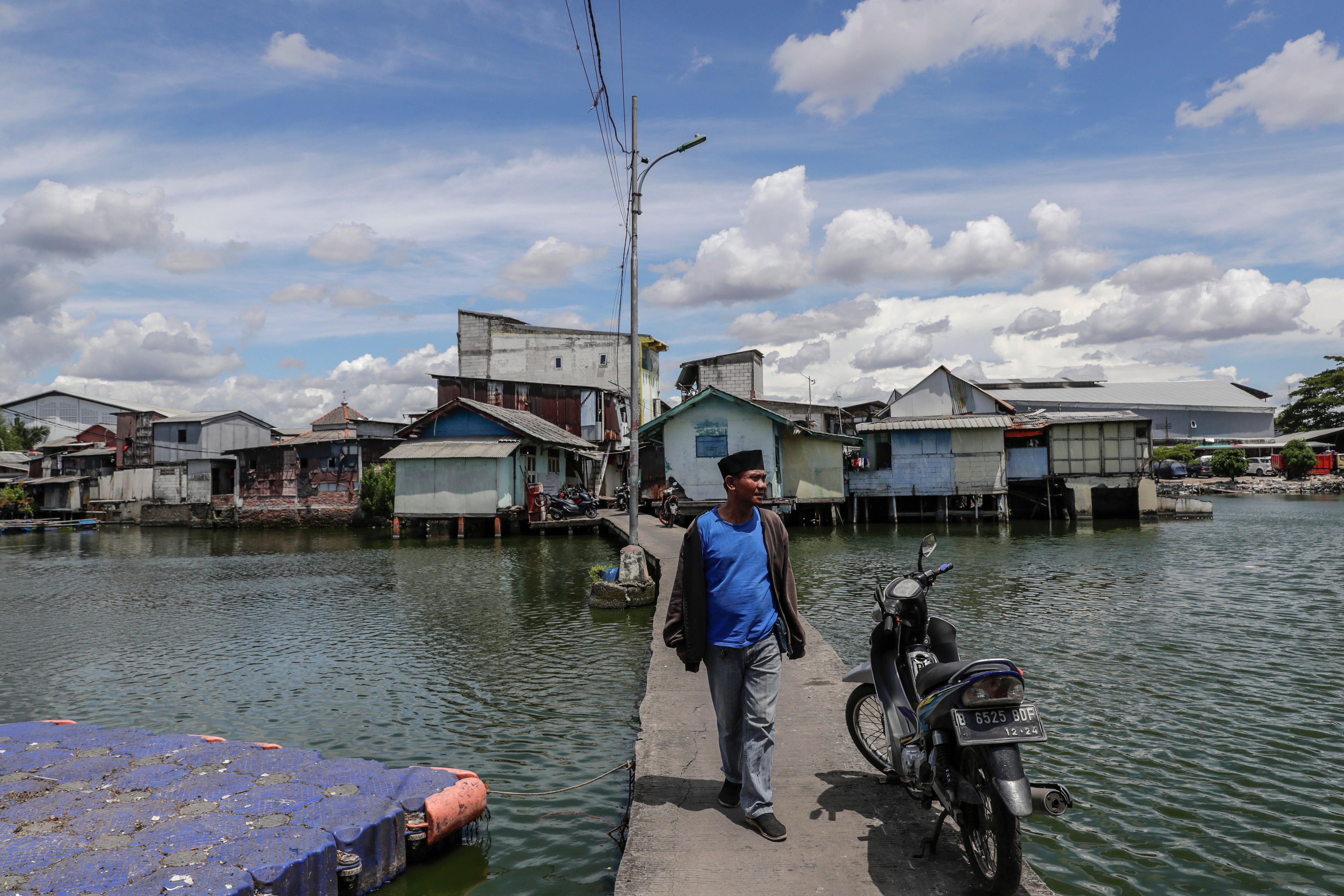 Susnandi Wahyu Budiawan Alatas walks on a path connecting the dry land with his floating village in Jakarta