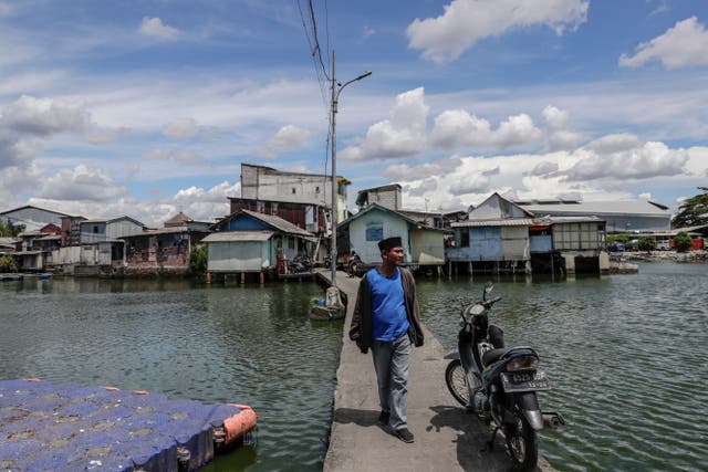 <p>Susnandi Wahyu Budiawan Alatas walks on a path connecting the dry land with his floating village in Jakarta</p>