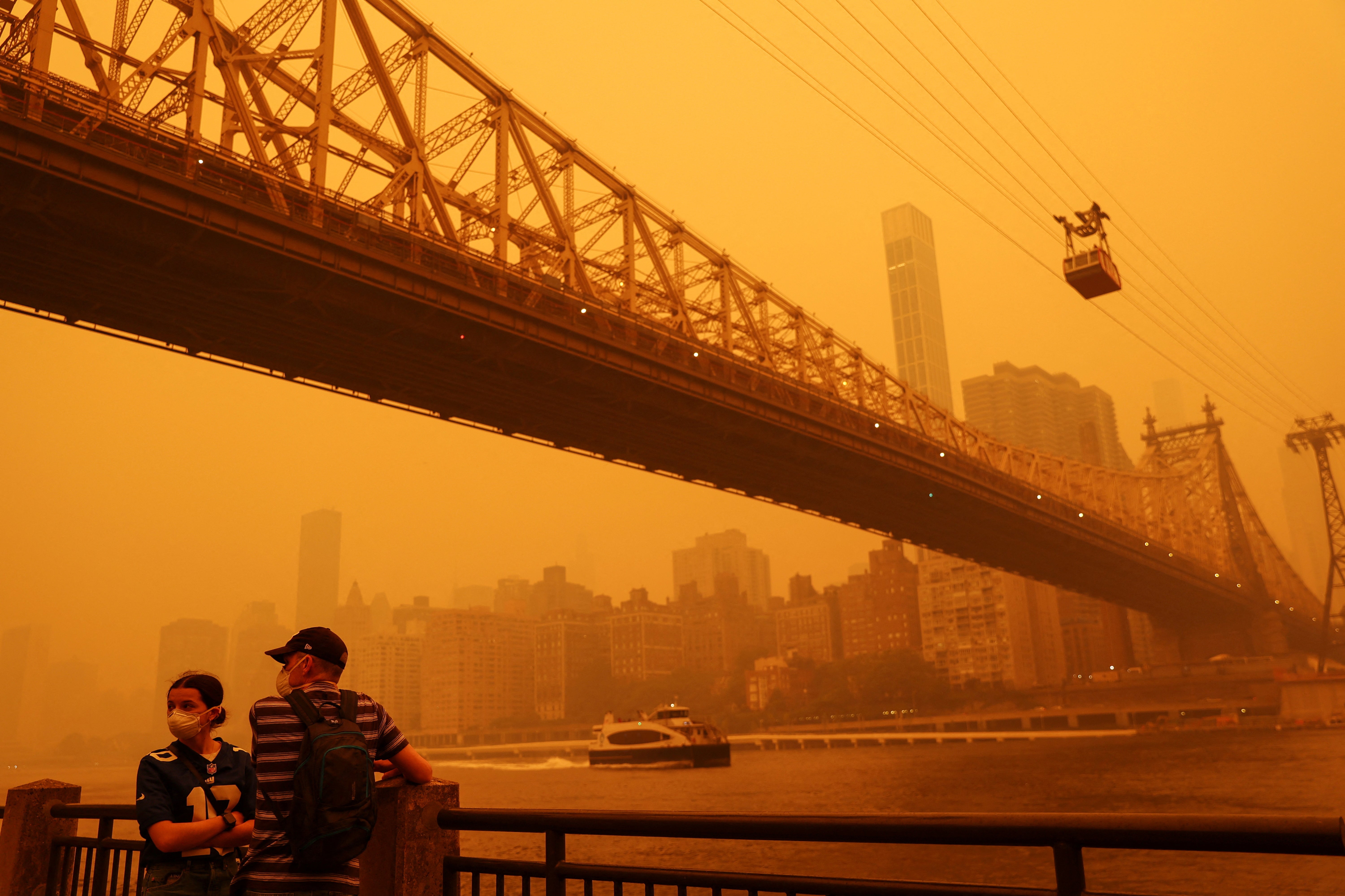 People wear protective masks as the Roosevelt Island Tram crosses the East River while haze and smoke from the Canadian wildfires shroud the Manhattan skyline