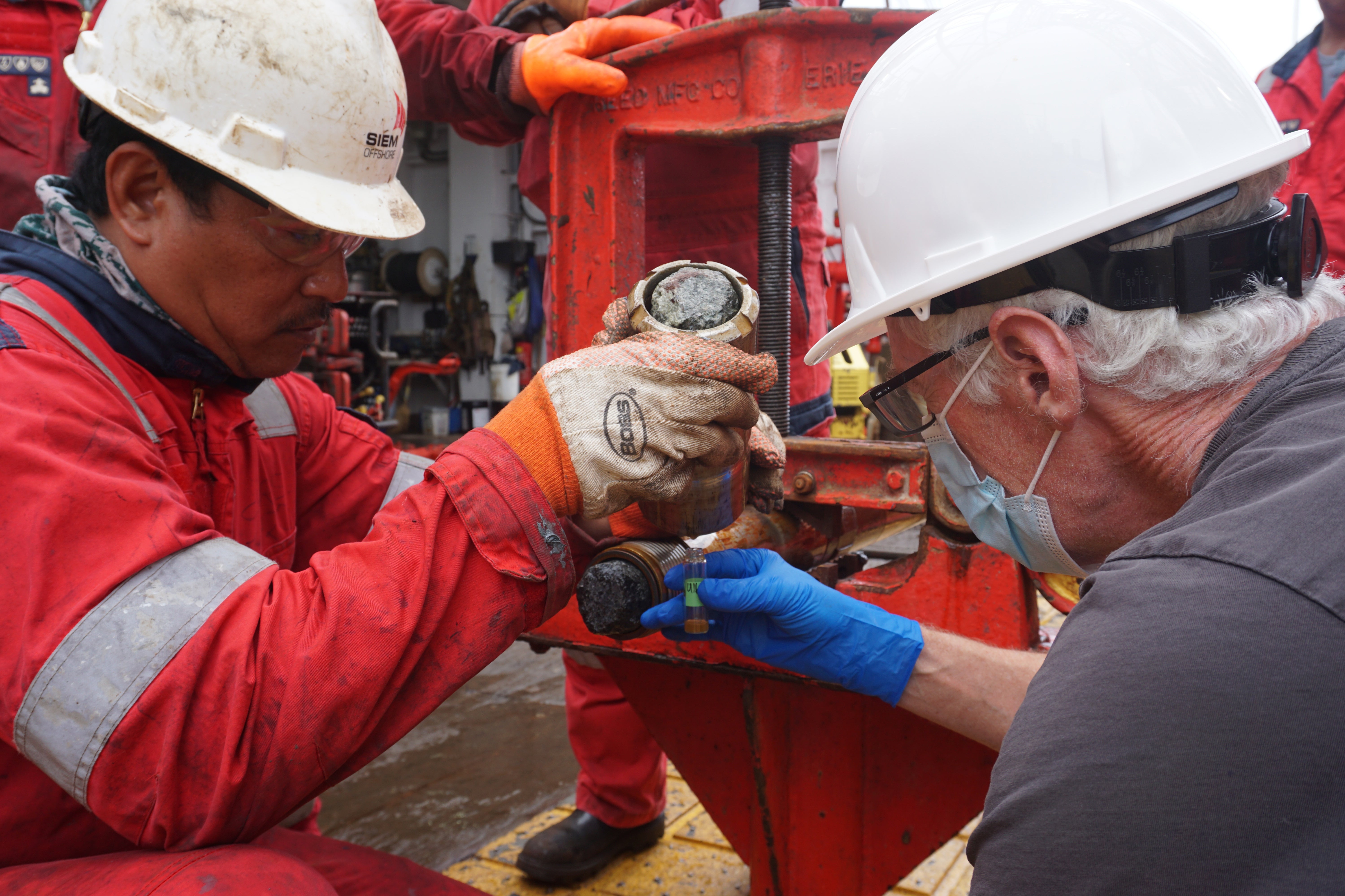 Gordon Southam, right, of the University of Queensland in Australia takes a fluid sample from the core catcher aboard the Joides Resolution