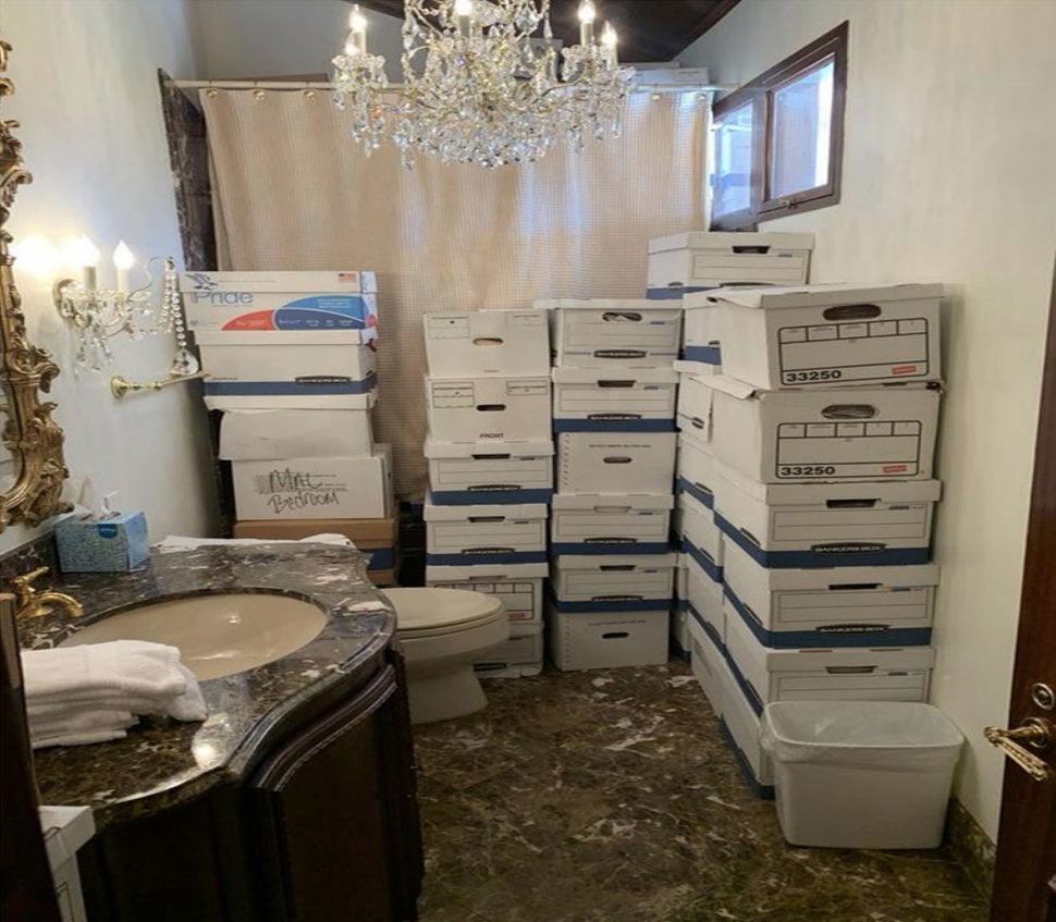 <p>Towers of boxes containing classified material in a bathroom underneath a chandelier </p>