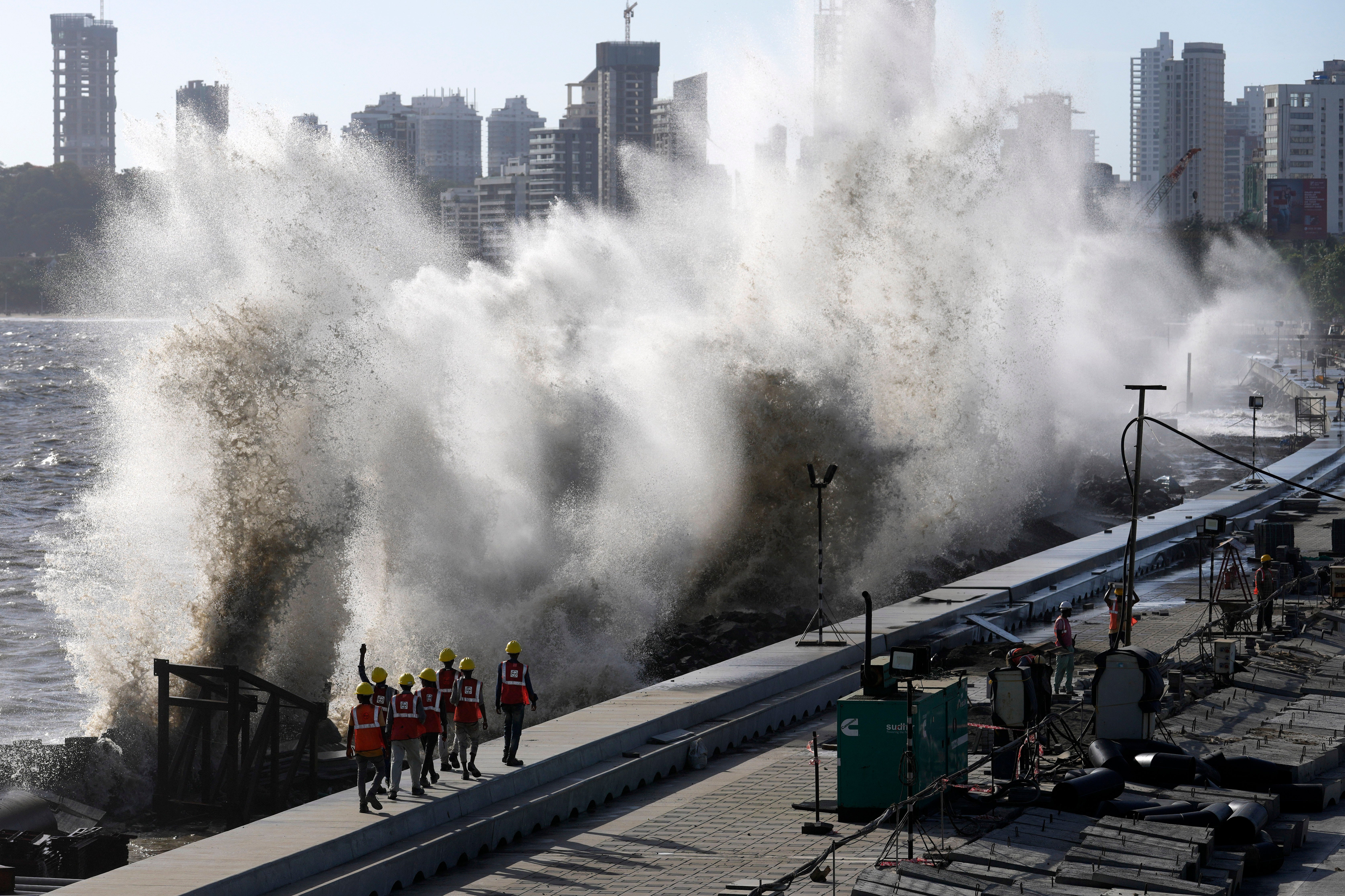 Coastal road workers walk as waves hit the city’s waterfront during high tide in the Arabian Sea at Marine Drive in Mumbai
