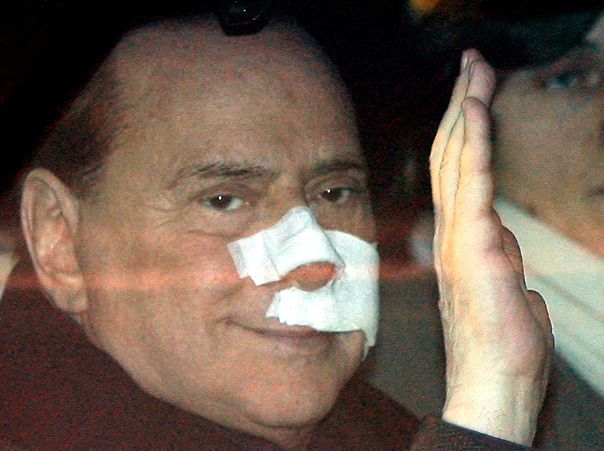 Berlusconi waves from his car as he arrives at his home, with his face covered in bandages, four days after an attack at a political rally in December 2009
