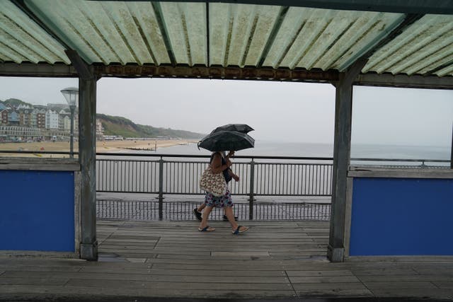 People take shelter beneath umbrellas as they walk in the rain along Boscombe Pier in Dorset (Andrew Matthews/PA)
