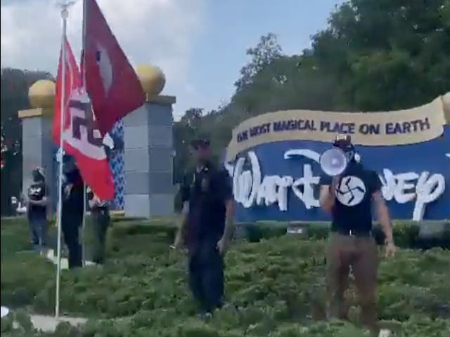<p>A protester in a swastika t-shirt uses a megaphone in front of Walt Disney World in Florida while Nazi flags fly to his right</p>