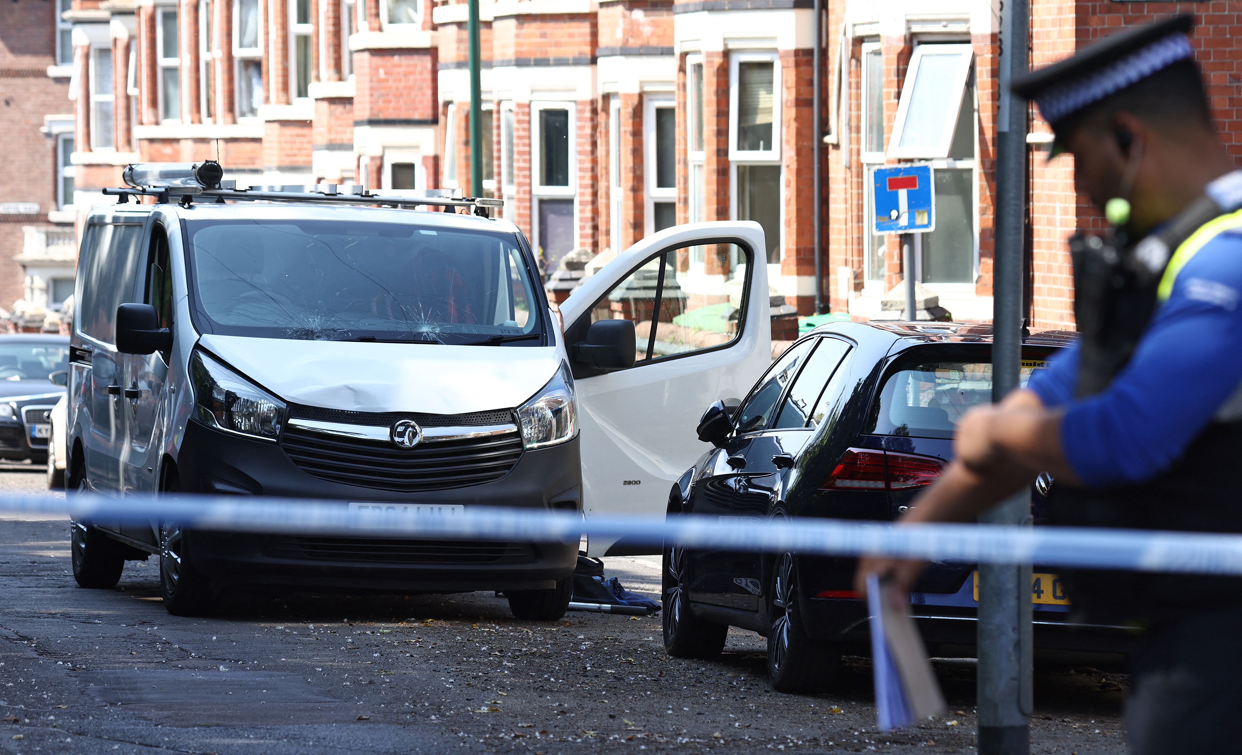 A police officer stands on duty by a white van with a shattered windscreen, inside a cordon on Bentinck Road in Nottingham