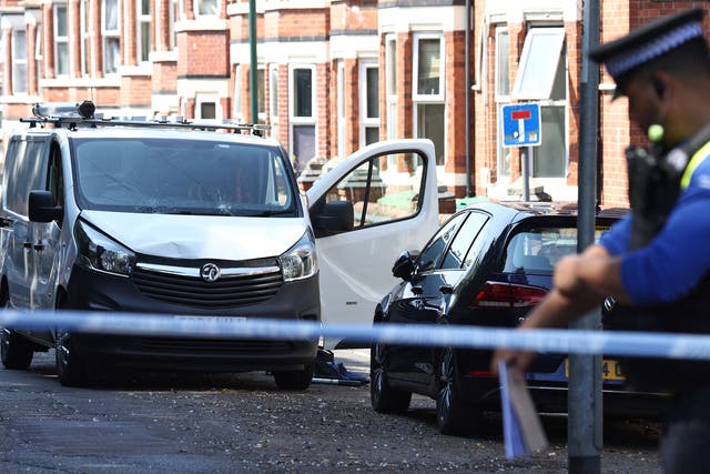 <p>A police officer stands on duty by a white van with a shattered windscreen, inside a cordon on Bentinck Road in Nottingham</p>
