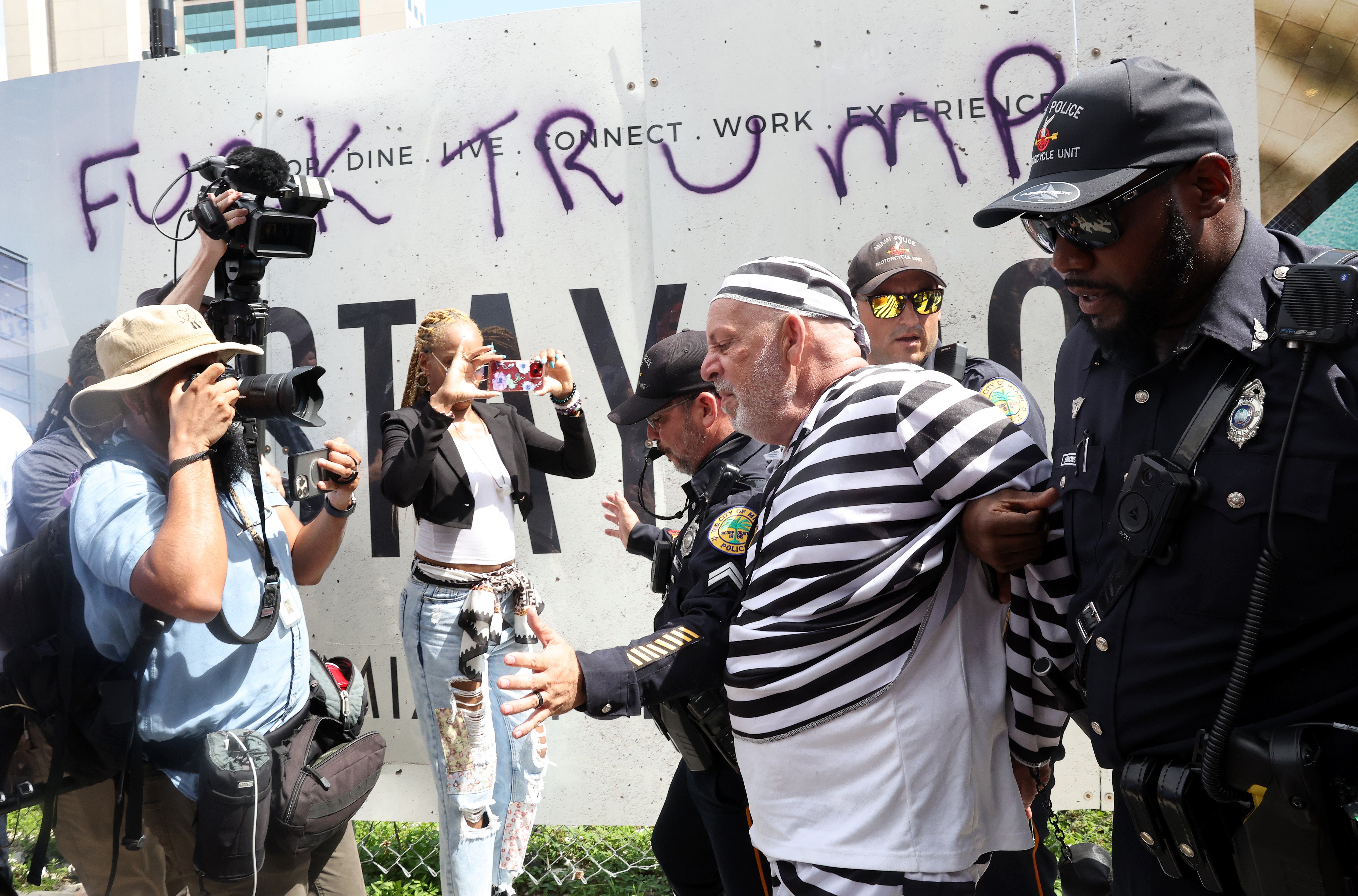 Protester Dominic Santana is detained by Miami Police officers after attempting to rush former President Donald Trump's motorcade