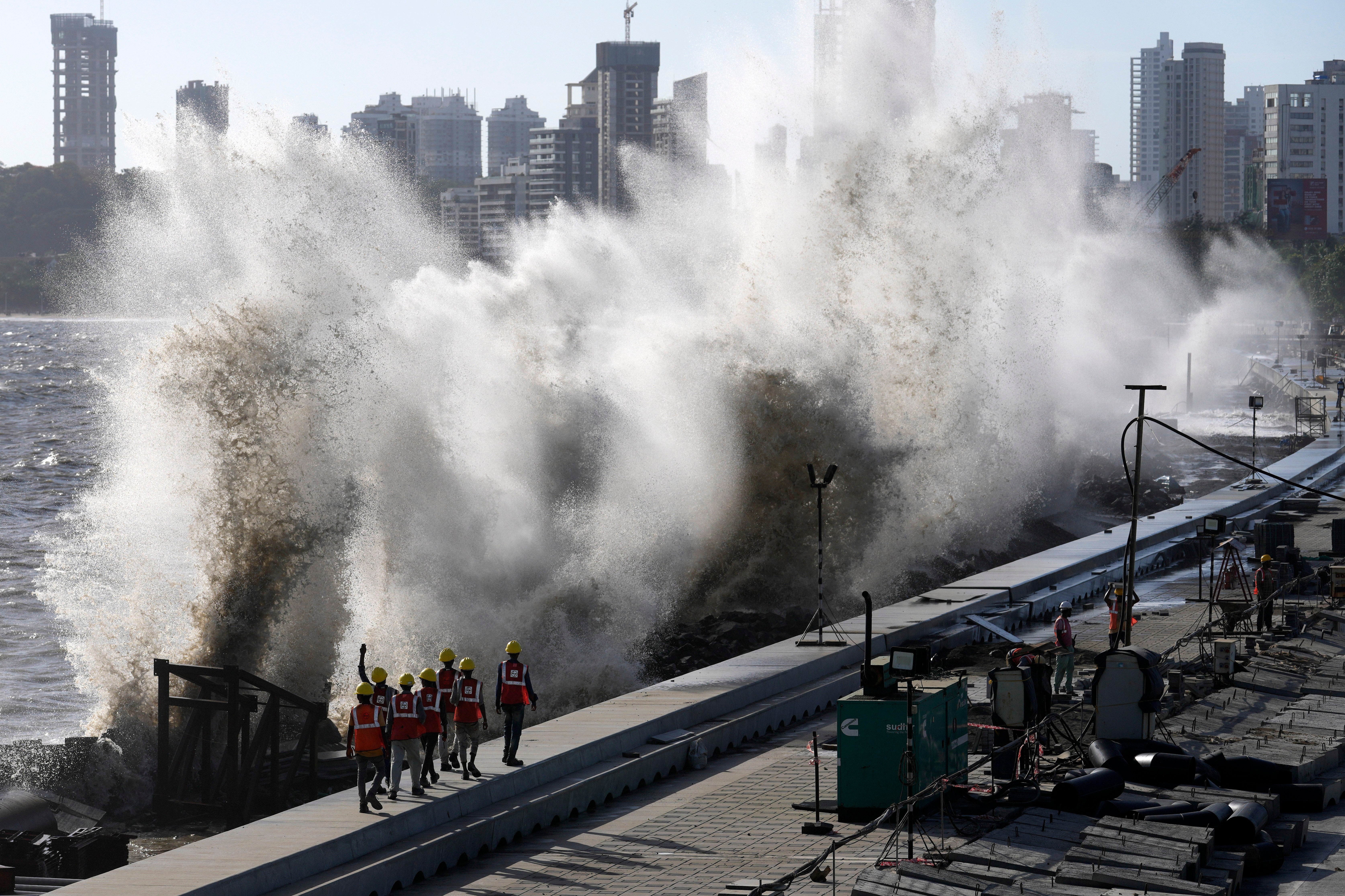 Coastal road workers walk as waves hit the city's waterfront during high tide in the Arabian Sea at Marine Drive in Mumbai