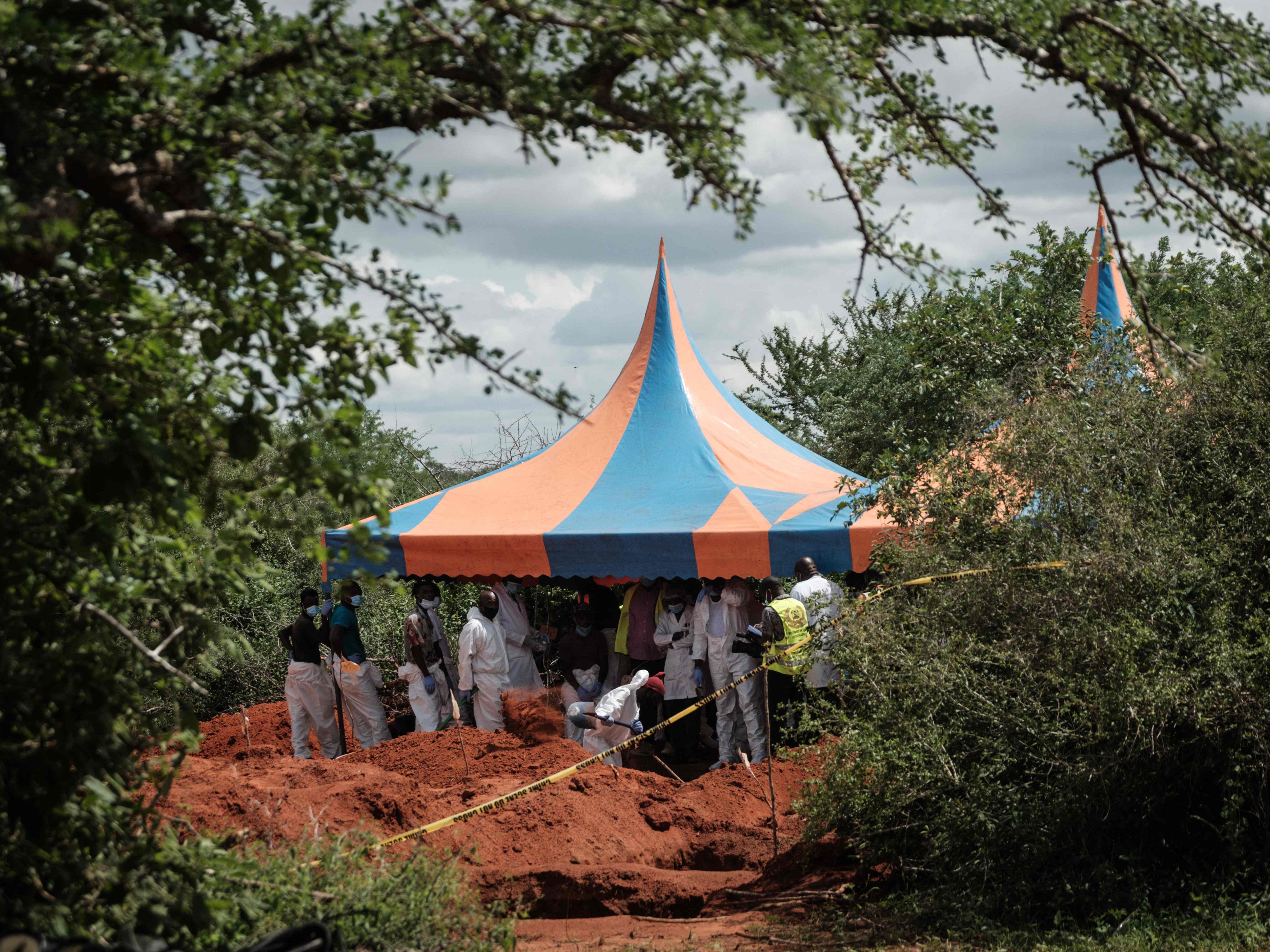 Workers take shelter while digging the ground to exume bodies from the mass grave site in the Shakahola forest of Malindi, Kenya