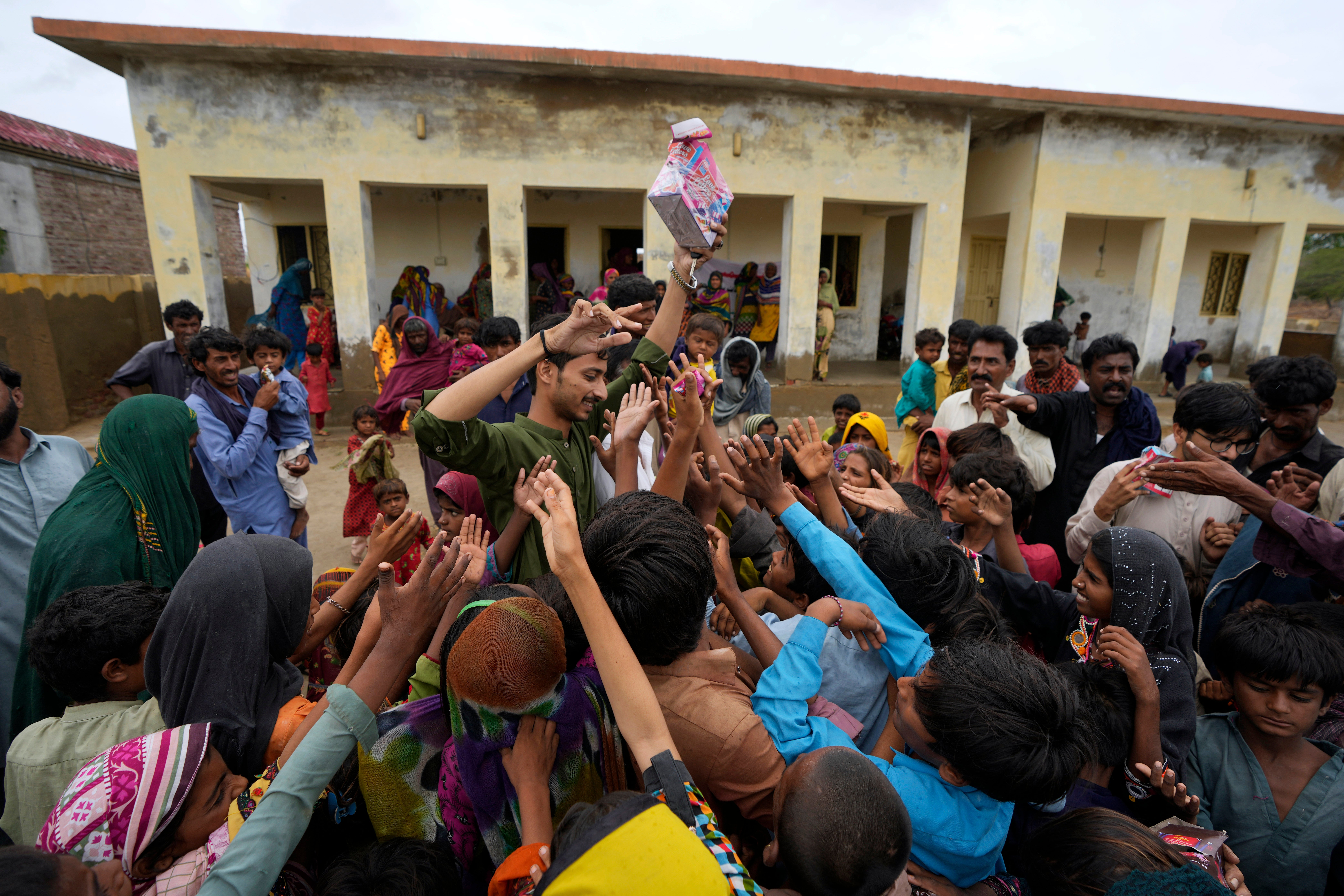 A volunteer distributes food items among children at a camp set up in a school building for internally displaced people from coastal areas, as Cyclone Biparjoy was approaching, in Badin, Pakistan's southern district in the Sindh province