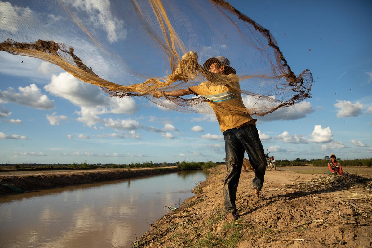 Farmer Deur Sok casts a fishing net across a canal facilitated by WFP in Sambour Commune, in Cambodia’s Kampong Thom province