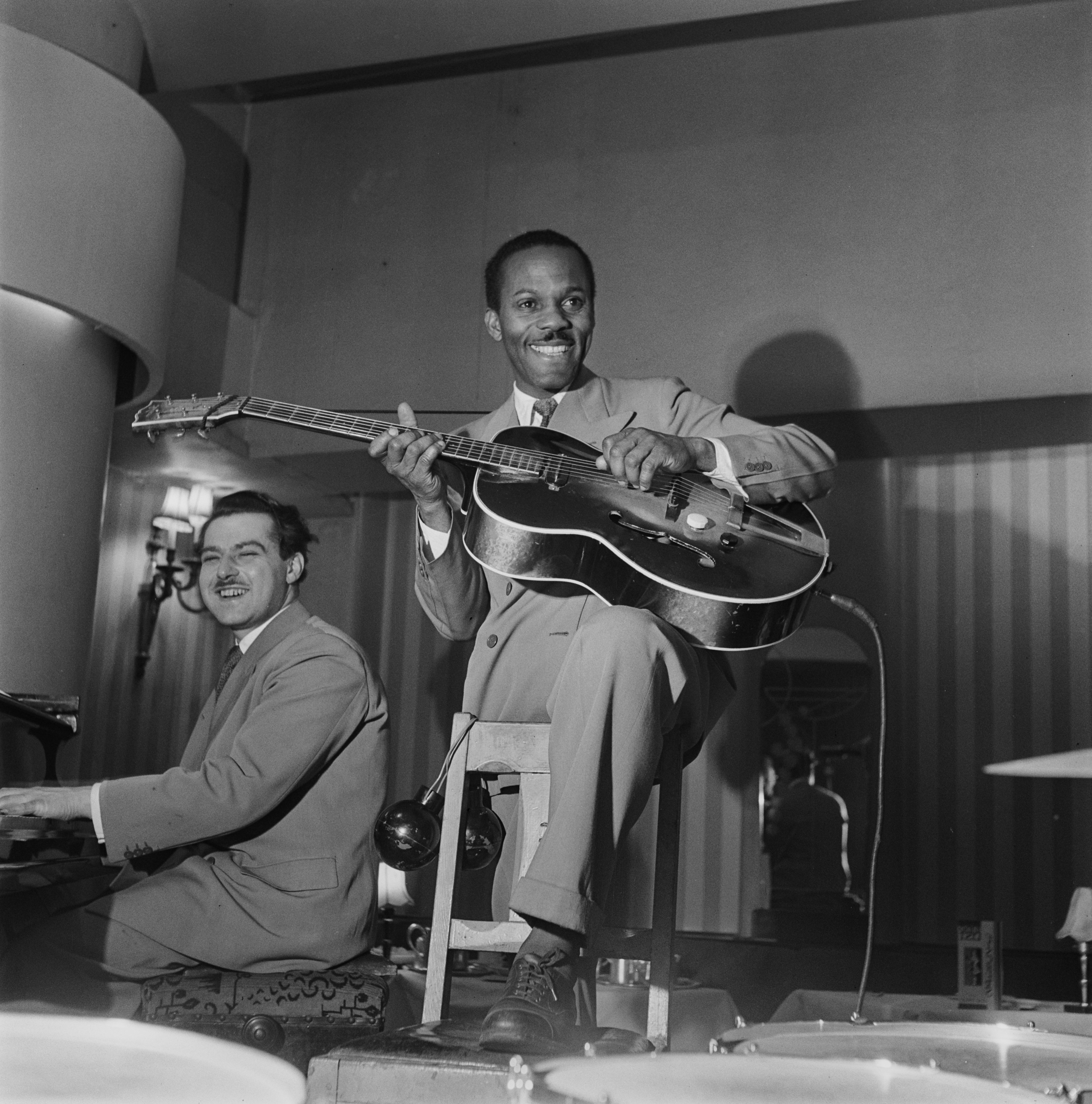 A musician plucking his electric guitar near a pianist as their jazz band performs in London, 1948