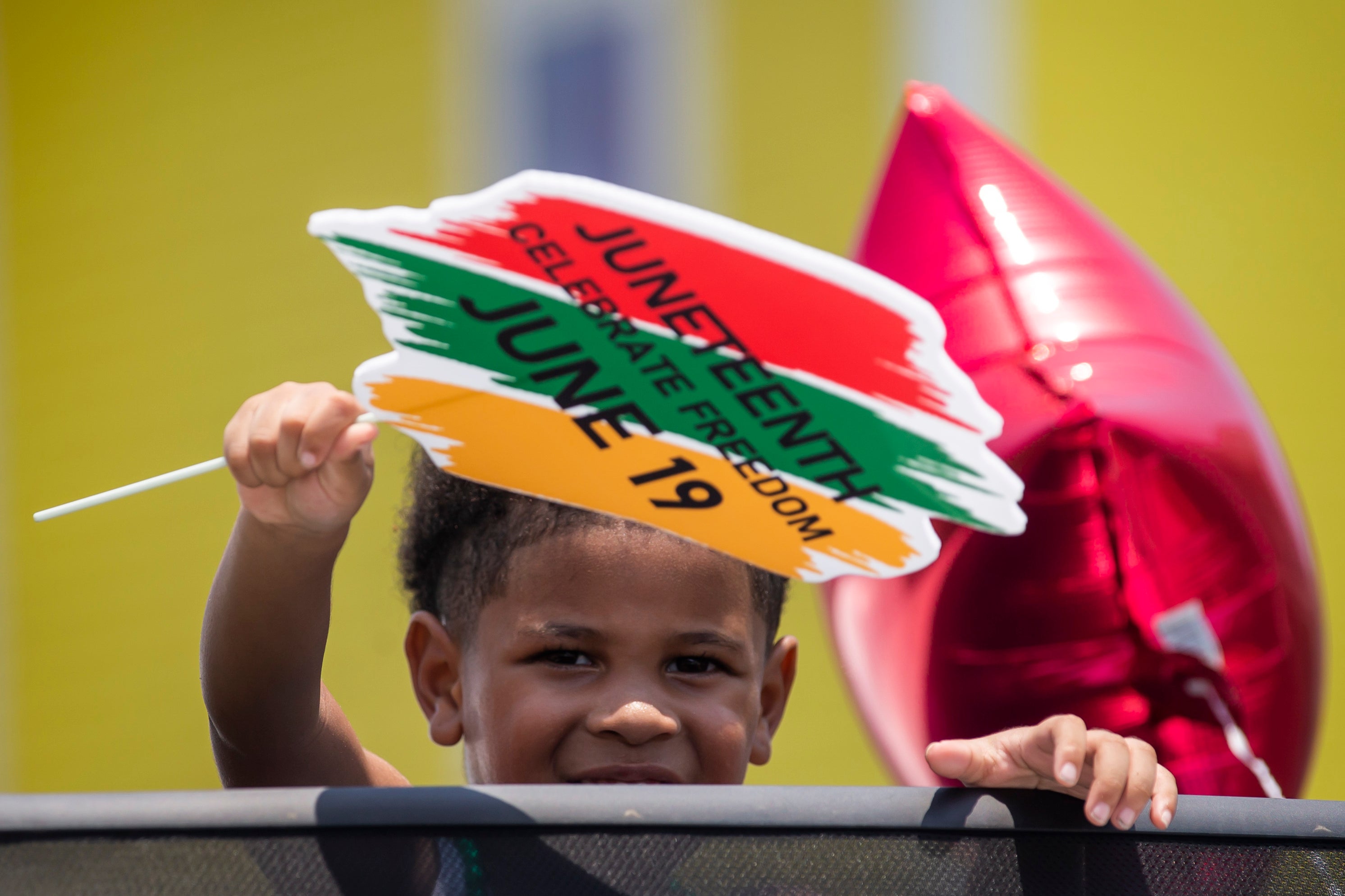 A young boy waves a Juneteenth sign from a car while riding in the annual Galveston Juneteenth Parade in Galveston, Texas