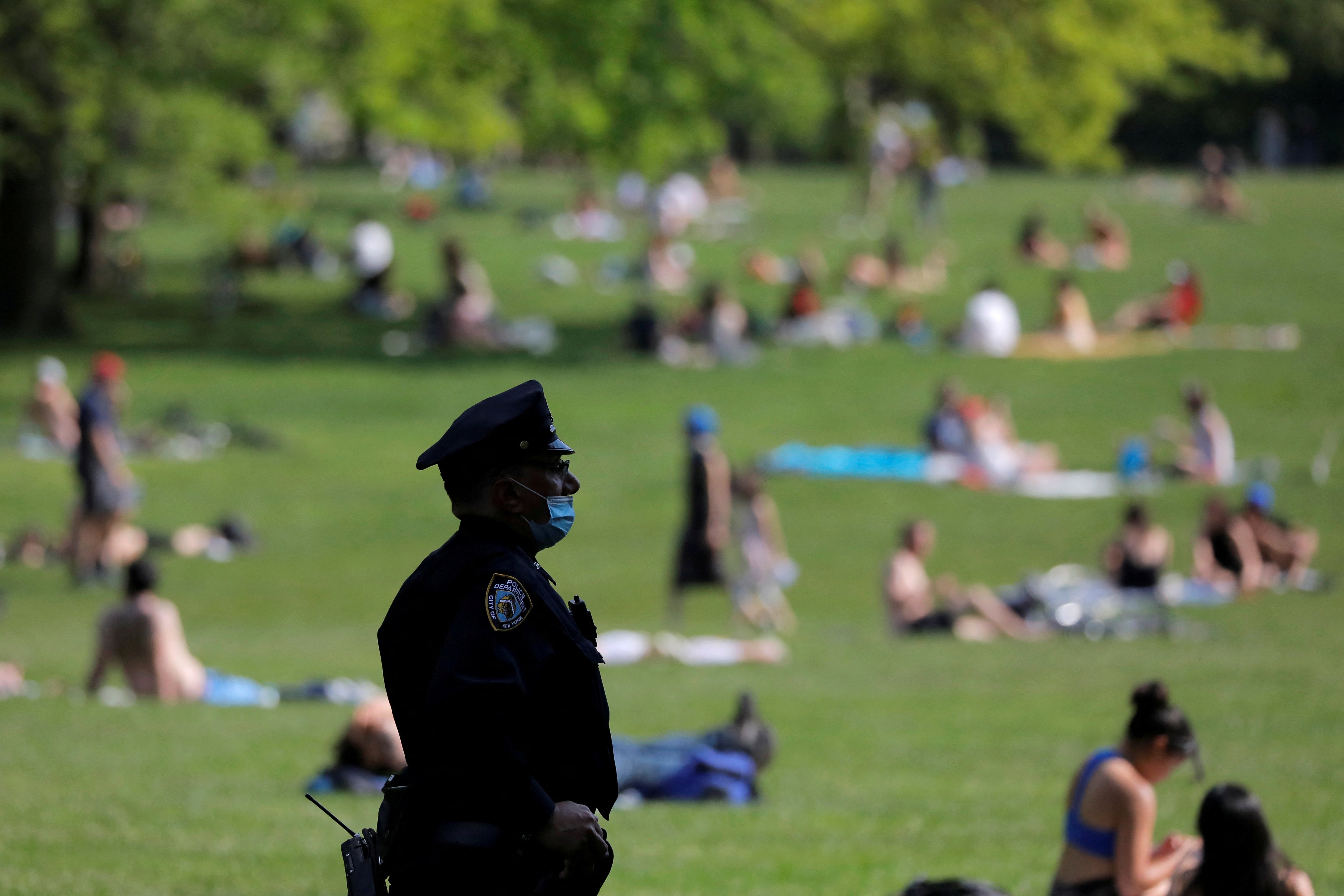 <p>A New York City Police Department officer wearing a protective face mask watches as people gather in the Sheep Meadow in Central Park </p>