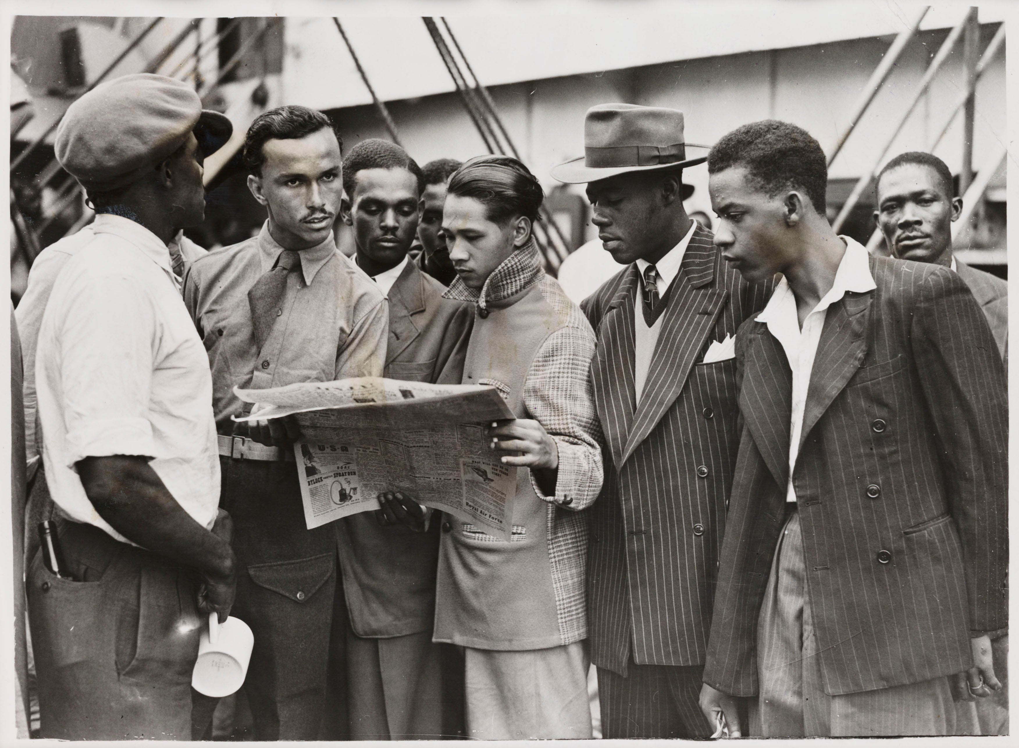 Passengers reading a newspaper whilst waiting to disembark from the ‘Empire Windrush’, having sailed from Jamaica