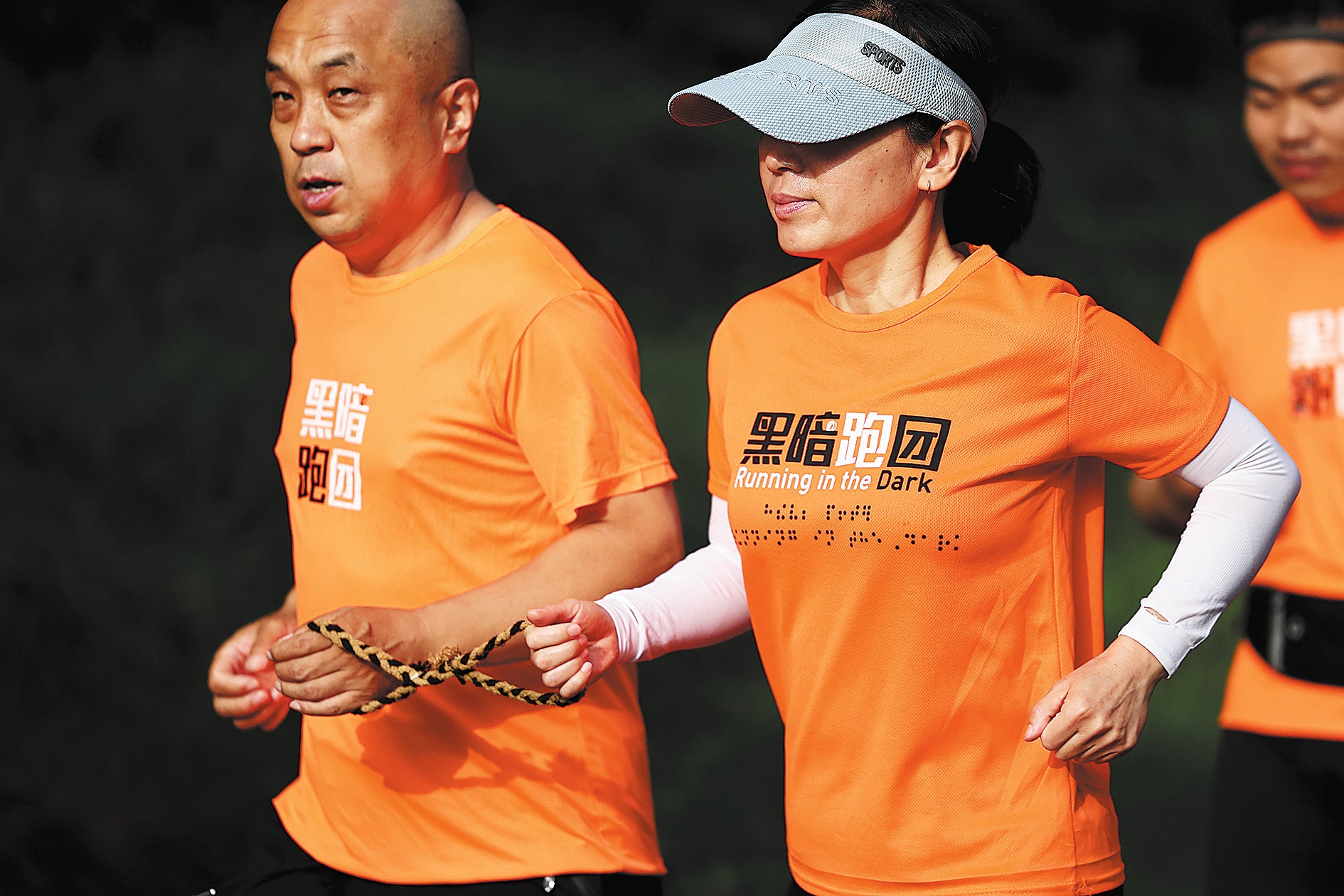 A volunteer guides a visually impaired runner with a hemp rope at the Beijing Olympic Forest Park