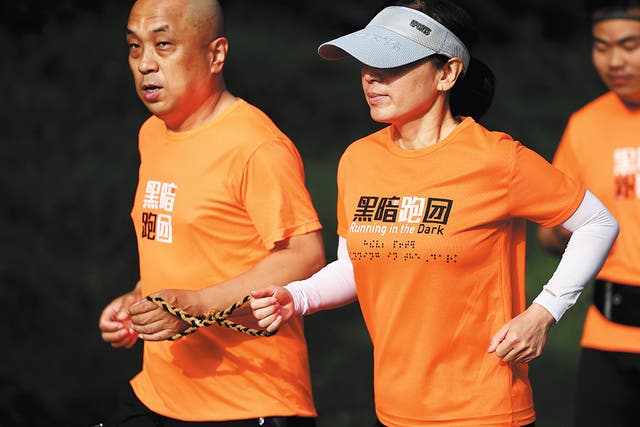 <p>A volunteer guides a visually impaired runner with a hemp rope at the Beijing Olympic Forest Park </p>
