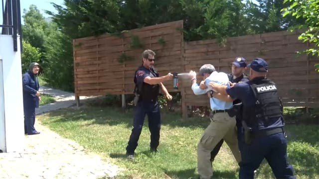 <p>An unidentified man is restrained by two police officers and sprayed with a nonlethal chemical weapon during a police raid on Ashraf III</p>