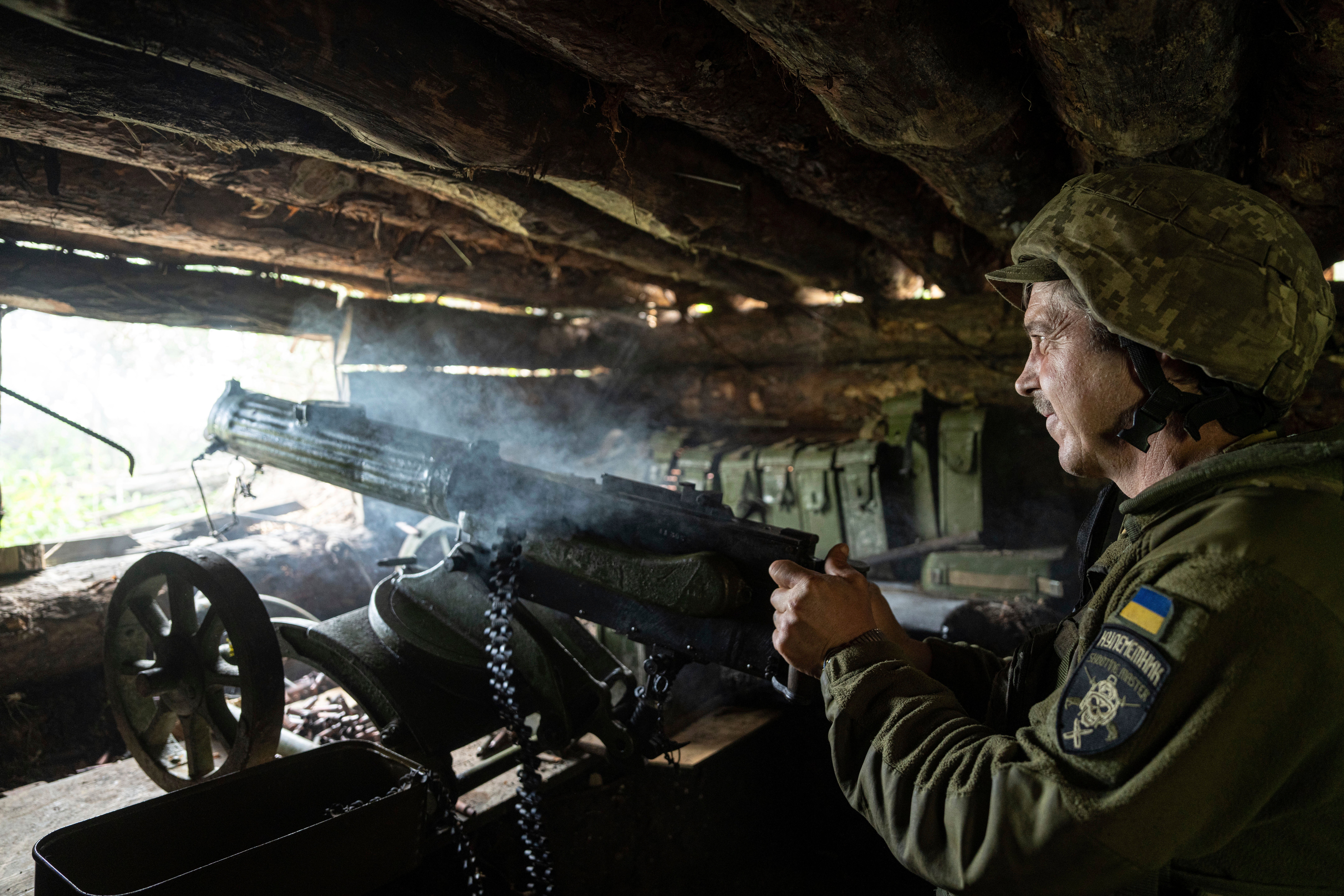 A Ukrainian 28th Brigade serviceman shoots a Maxim gun towards Russian positions at the front line in the eastern Donetsk region