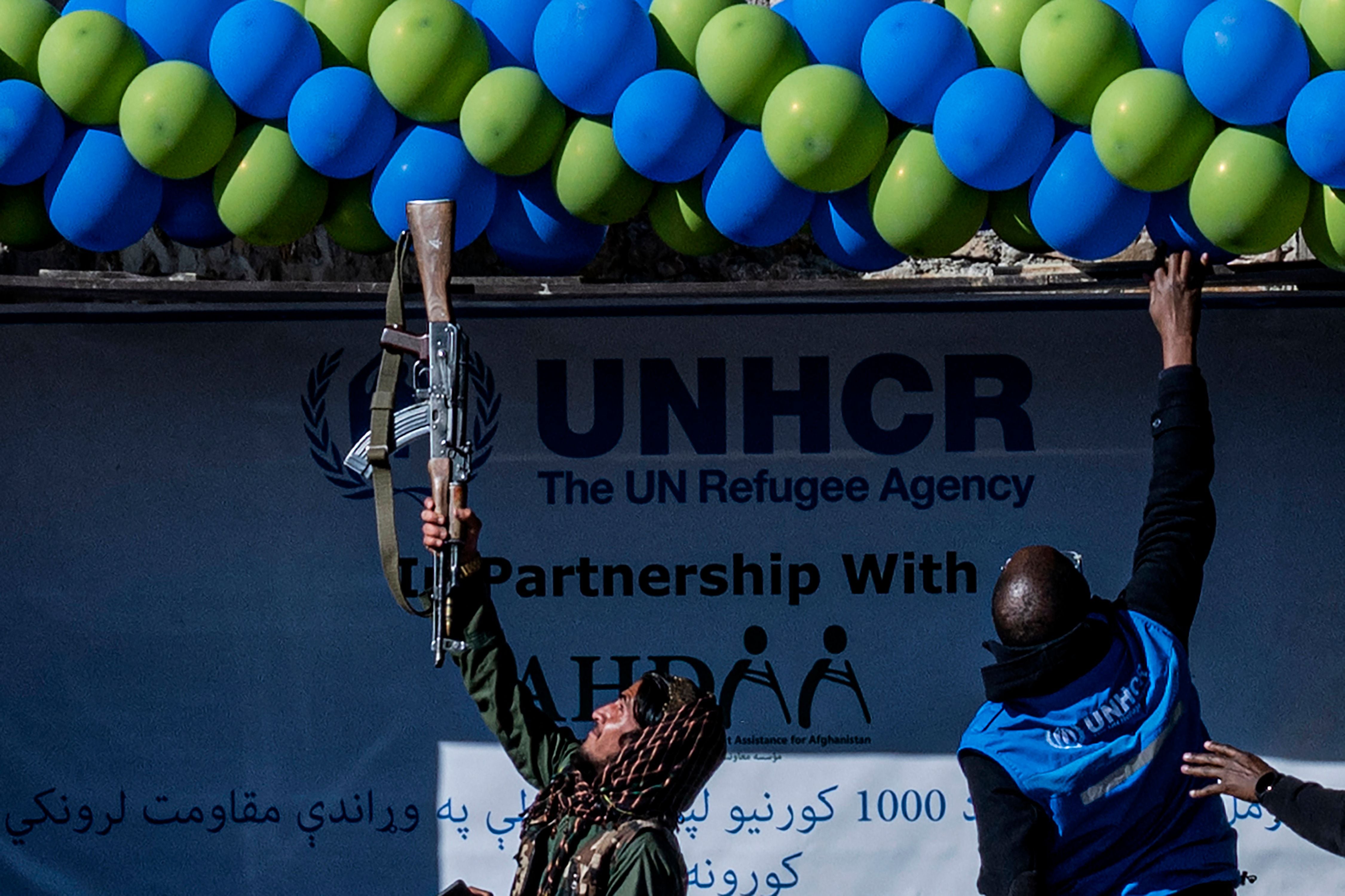 A member of Taliban security adjust balloons with his gun during a handover ceremony of newly built houses constructed by the United Nations refugee agency (UNHCR) in Paktika province