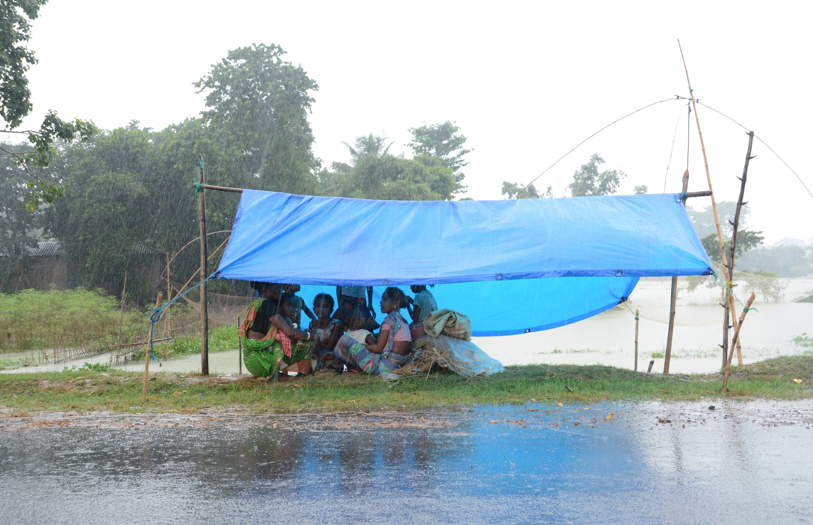Flood affected villagers sit under a temporary shelter during rainfall in a flood affected area in Morigaon district of Assam