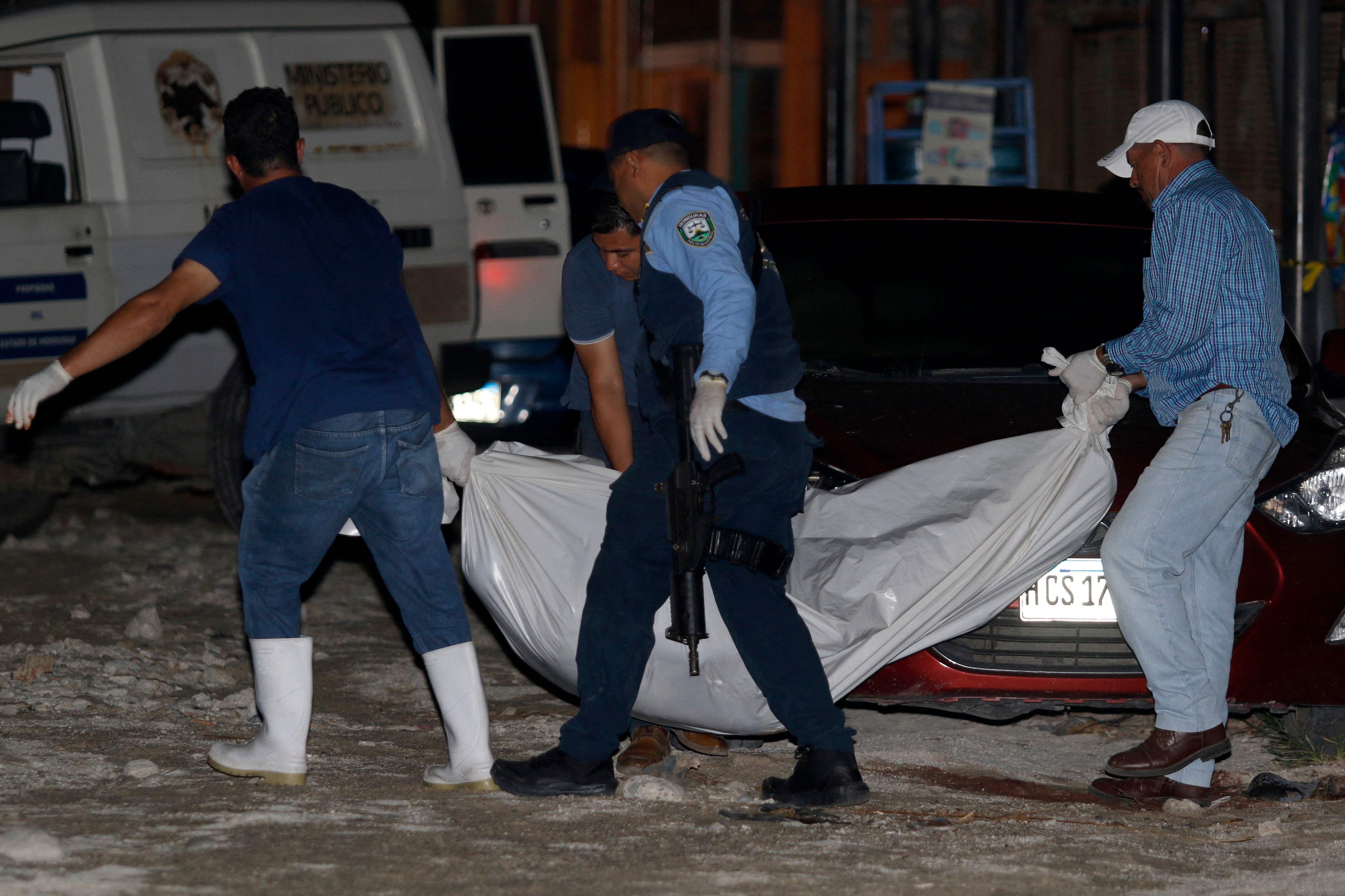 Forensic personnel and a police officer remove the body of one of the 13 people killed in a pool hall in Choloma