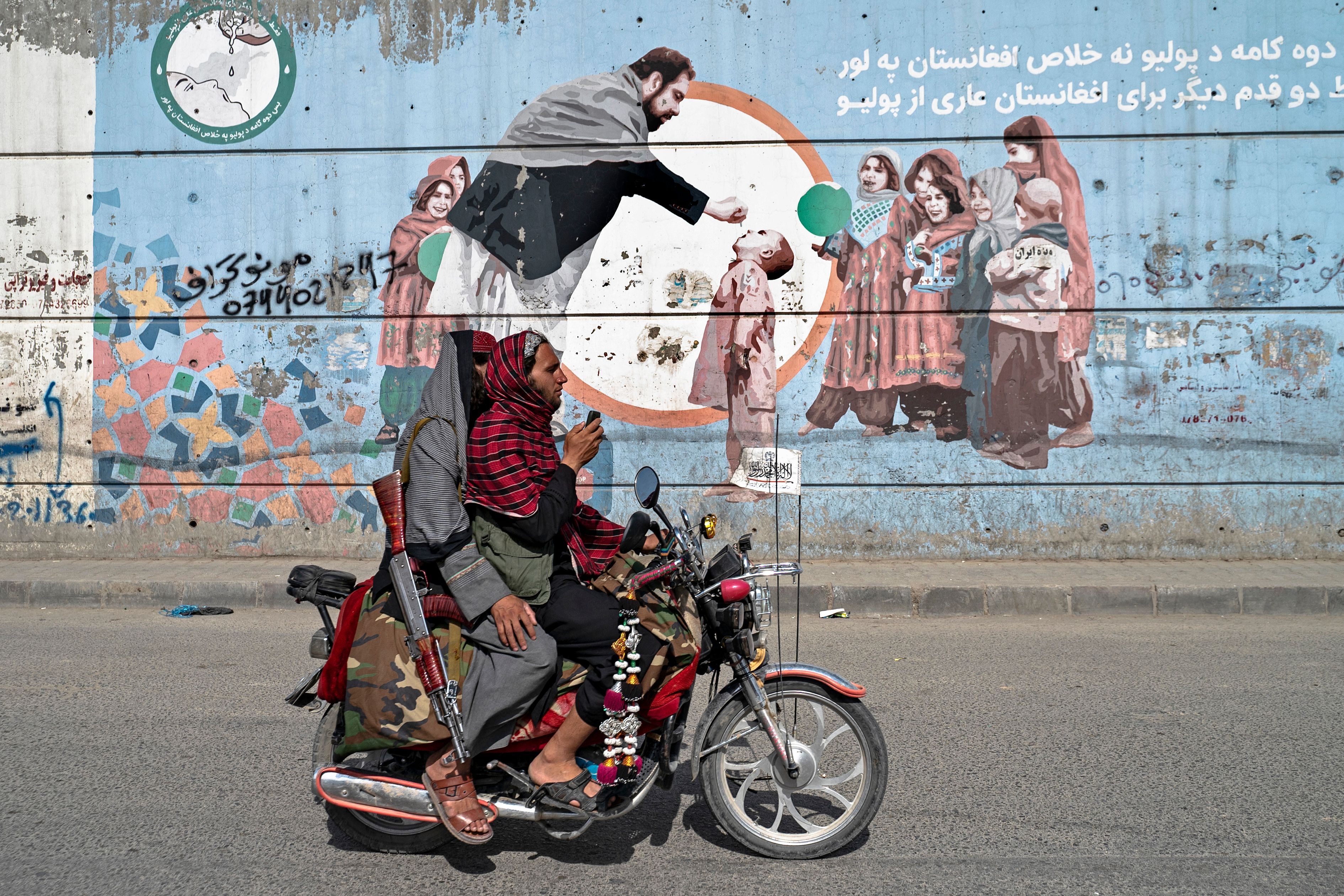 Taliban security personnel ride a motorcycle past a mural depicting polio vaccination campaign in Kabul