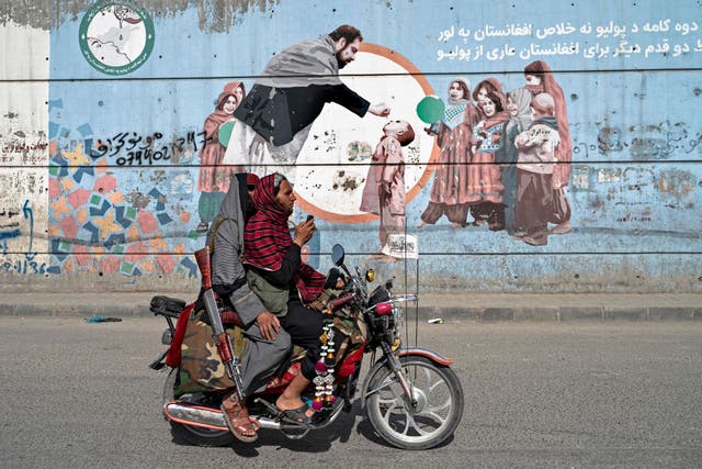<p>Taliban security personnel ride a motorcycle past a mural depicting polio vaccination campaign in Kabul</p>