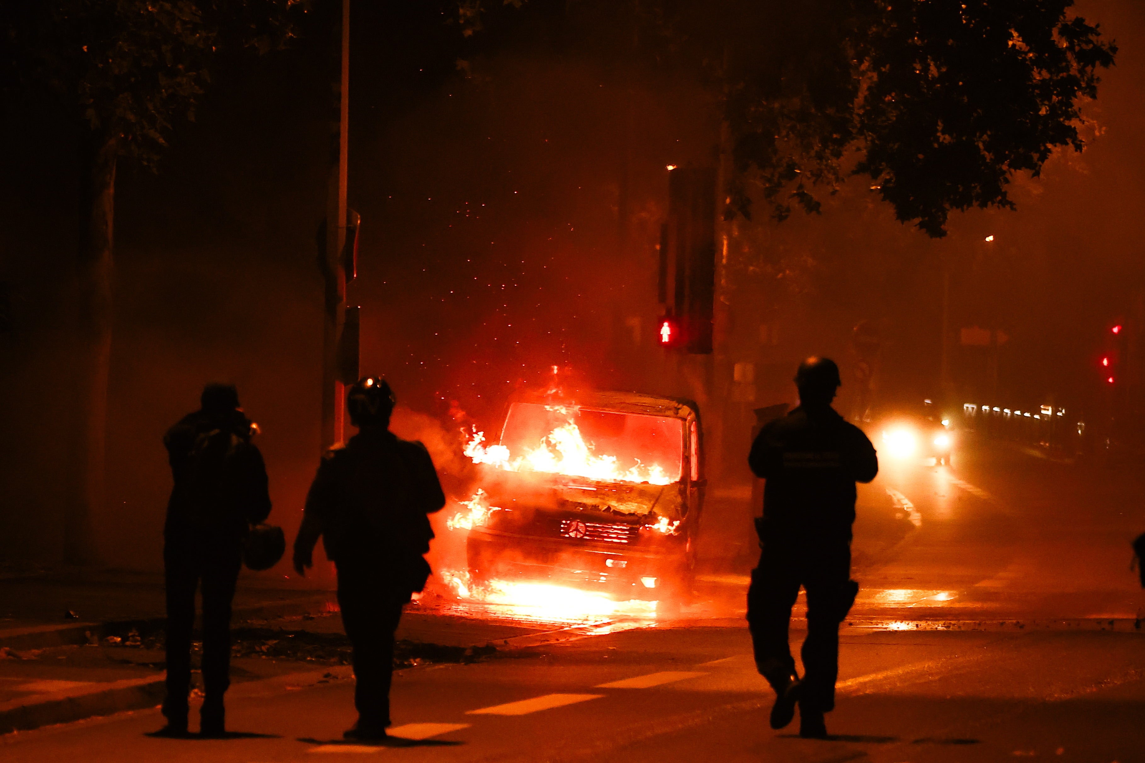 People walk next to a car burned during clashes between protesters and riot police in Nanterre