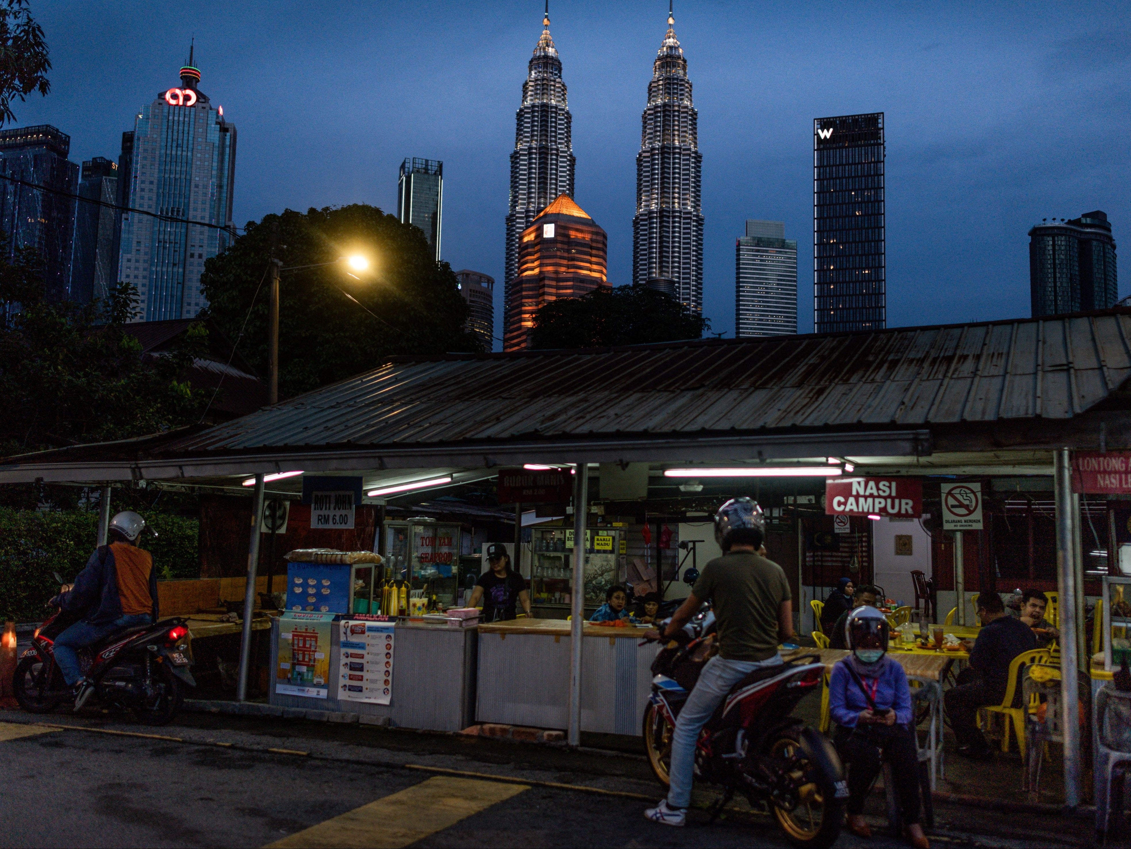 People buy food at a shop with Petronas Twin Towers (C) seen in the night skyline of Kuala Lumpur on 4 June 2020