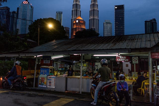 <p>People buy food at a shop with Petronas Twin Towers (C) seen in the night skyline of Kuala Lumpur on 4 June 2020</p>