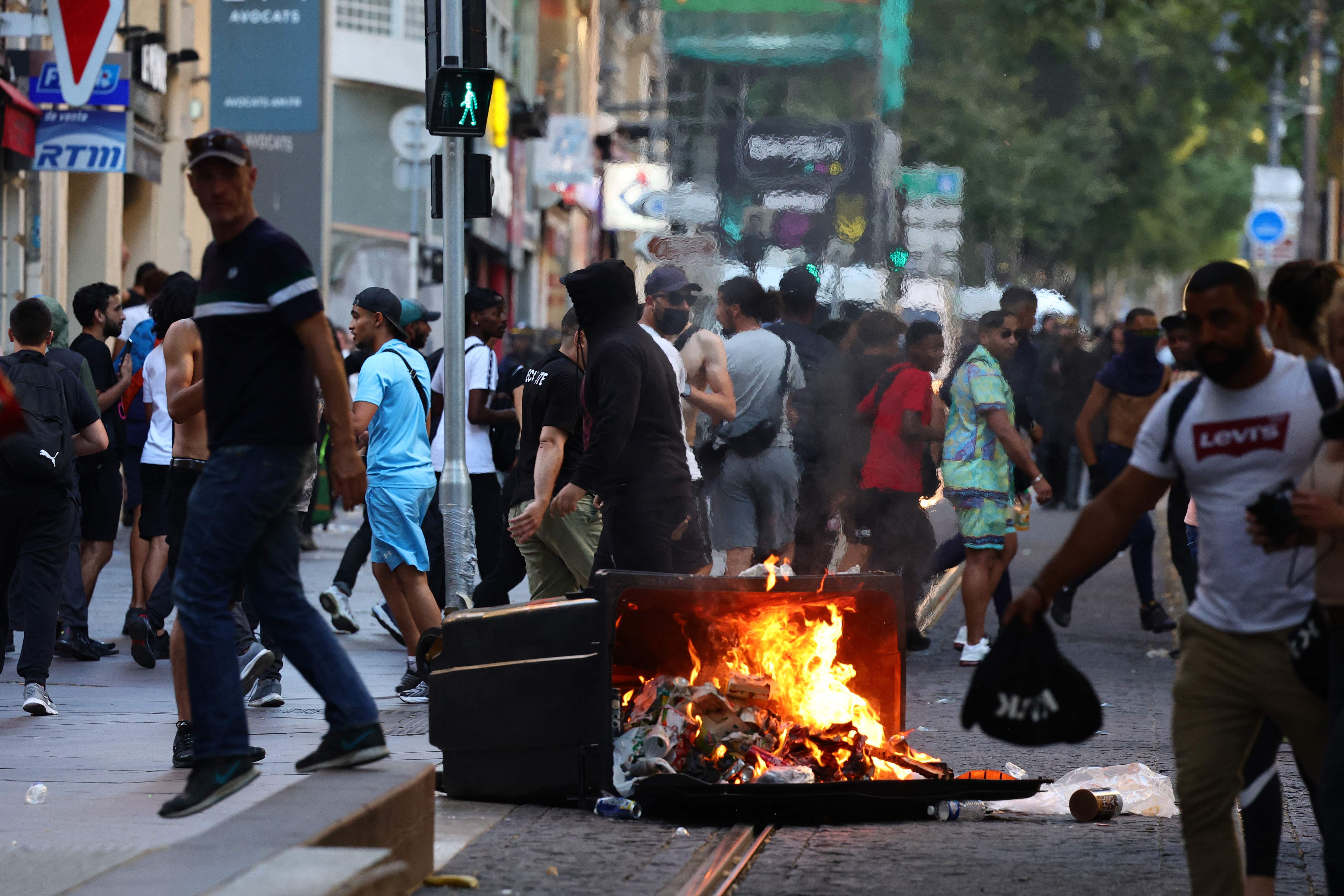 Protesters walk past a burnt out trash bin during clashes with police in Marseille