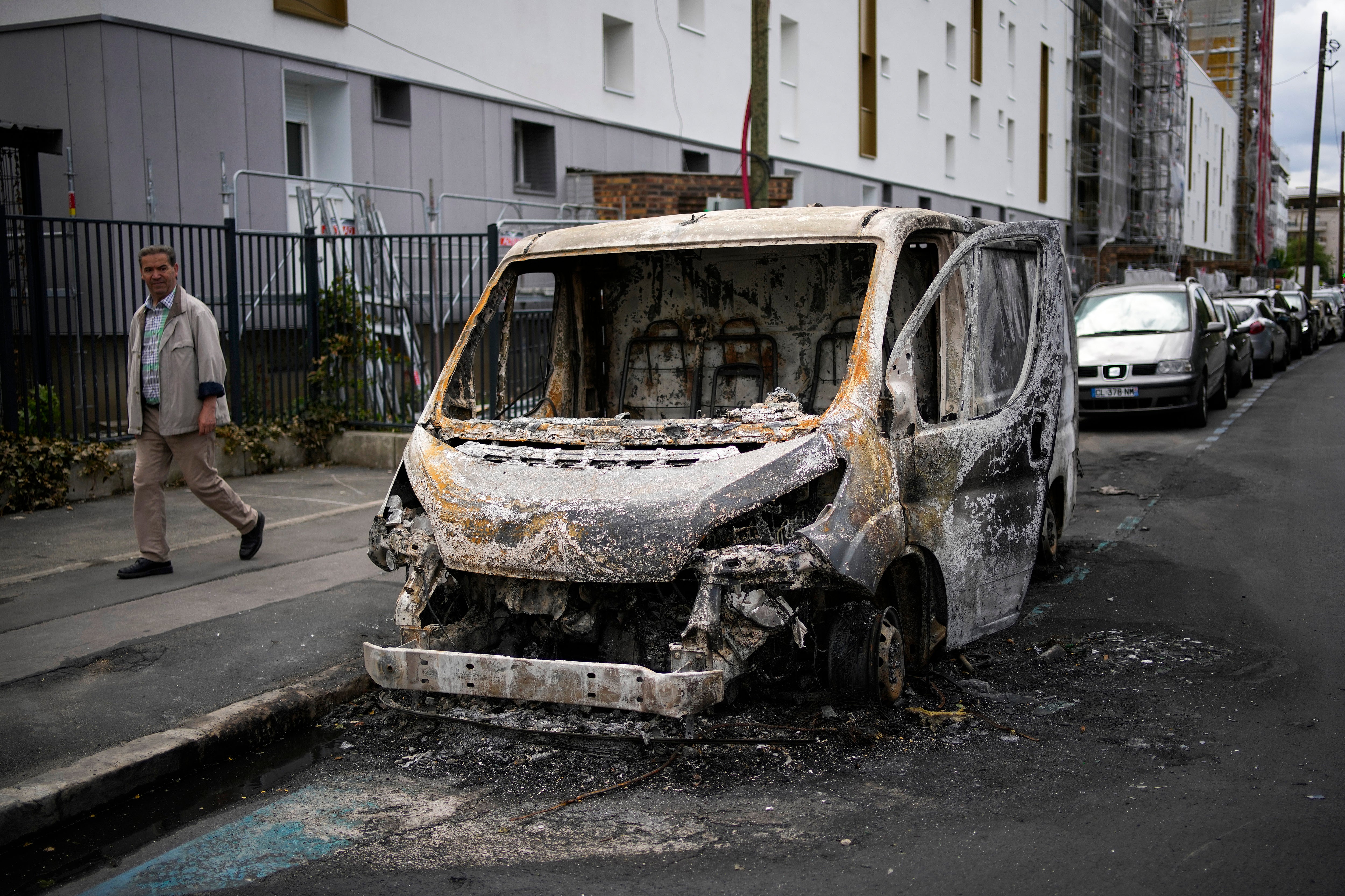 A man walks past a burned van on the aftermath of protests in Colombes, outside Paris on Saturday