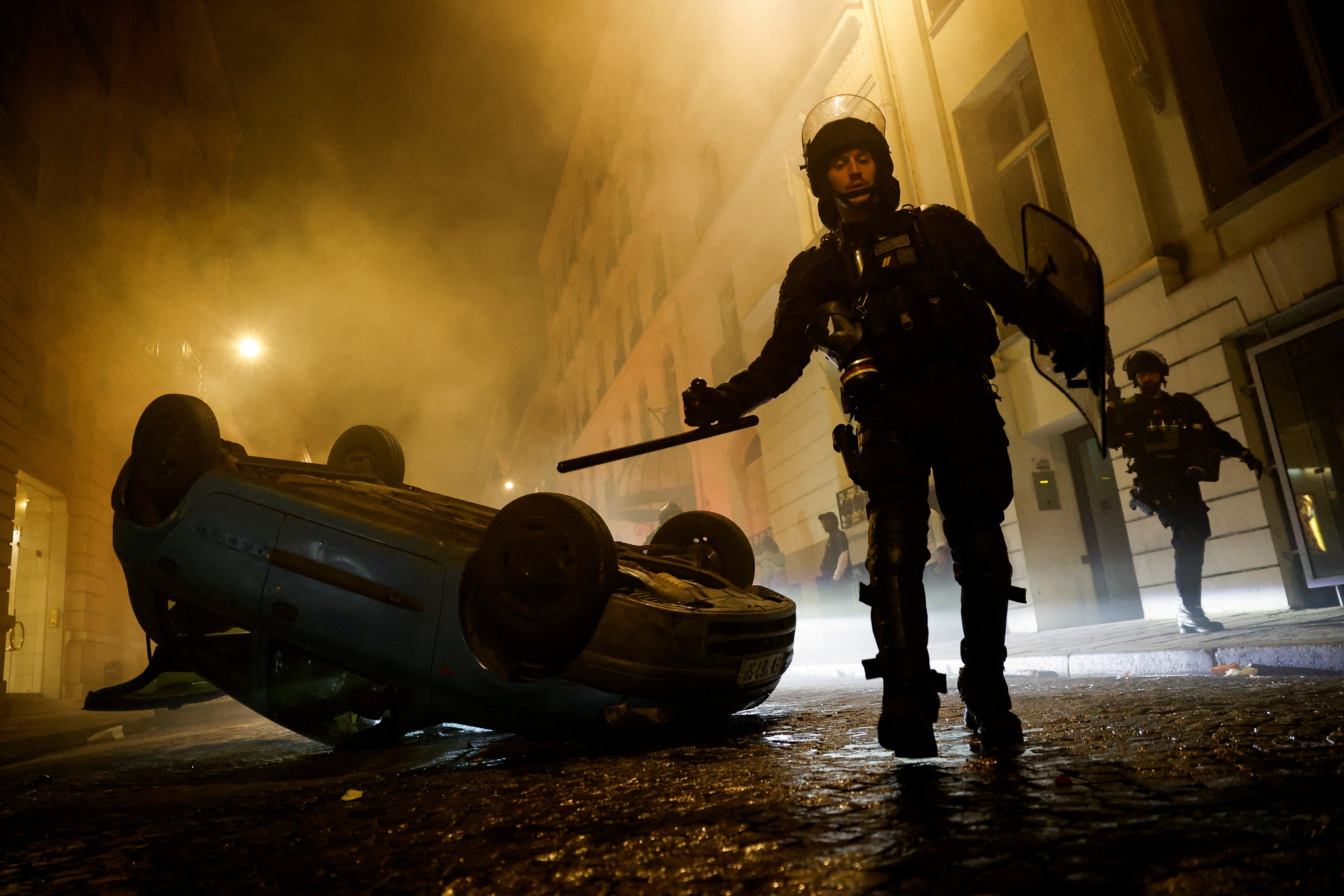 French riot police officers walk next to a vehicle upside down during the fifth day of protests