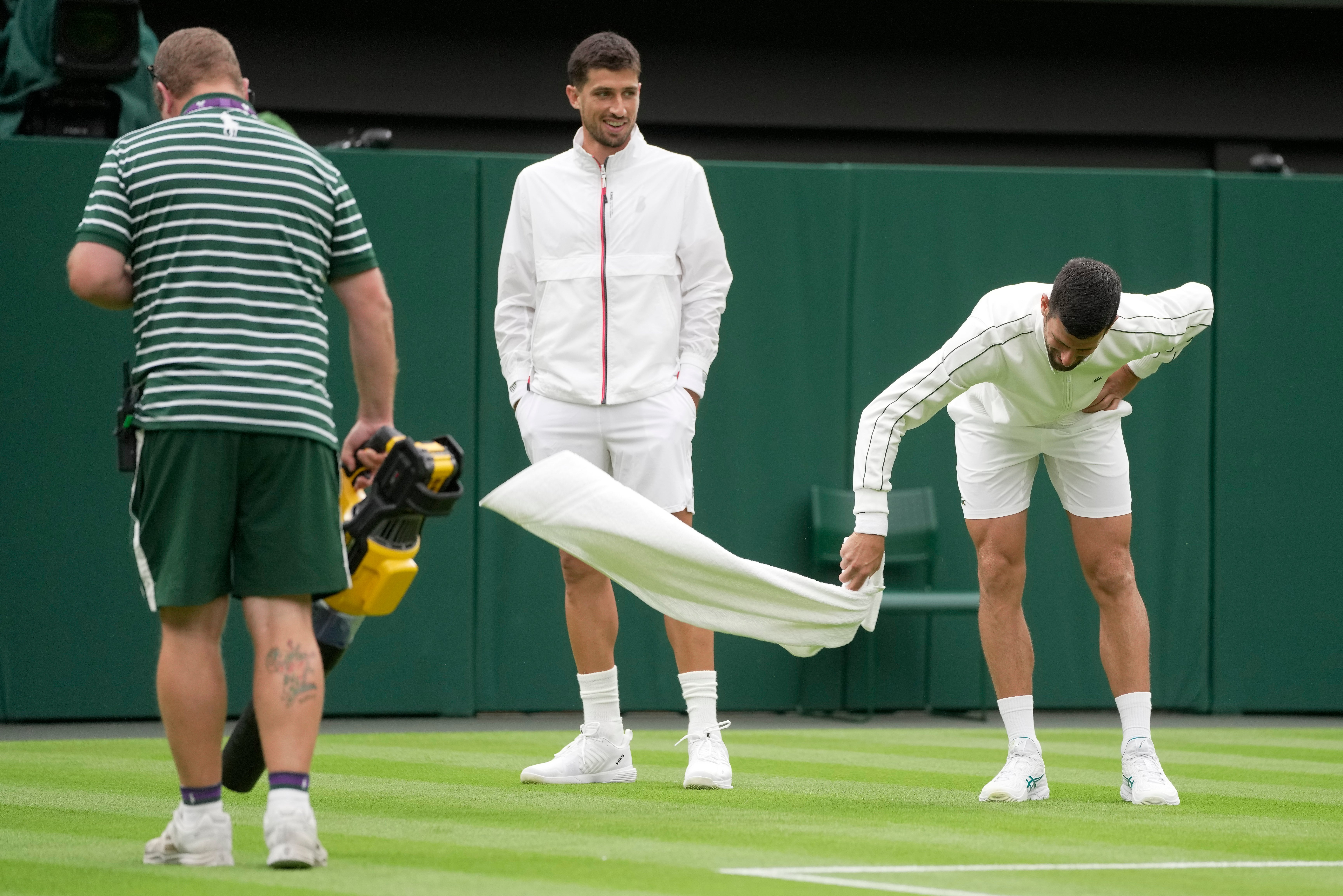 Djokovic attempts to dry the grass with a towel