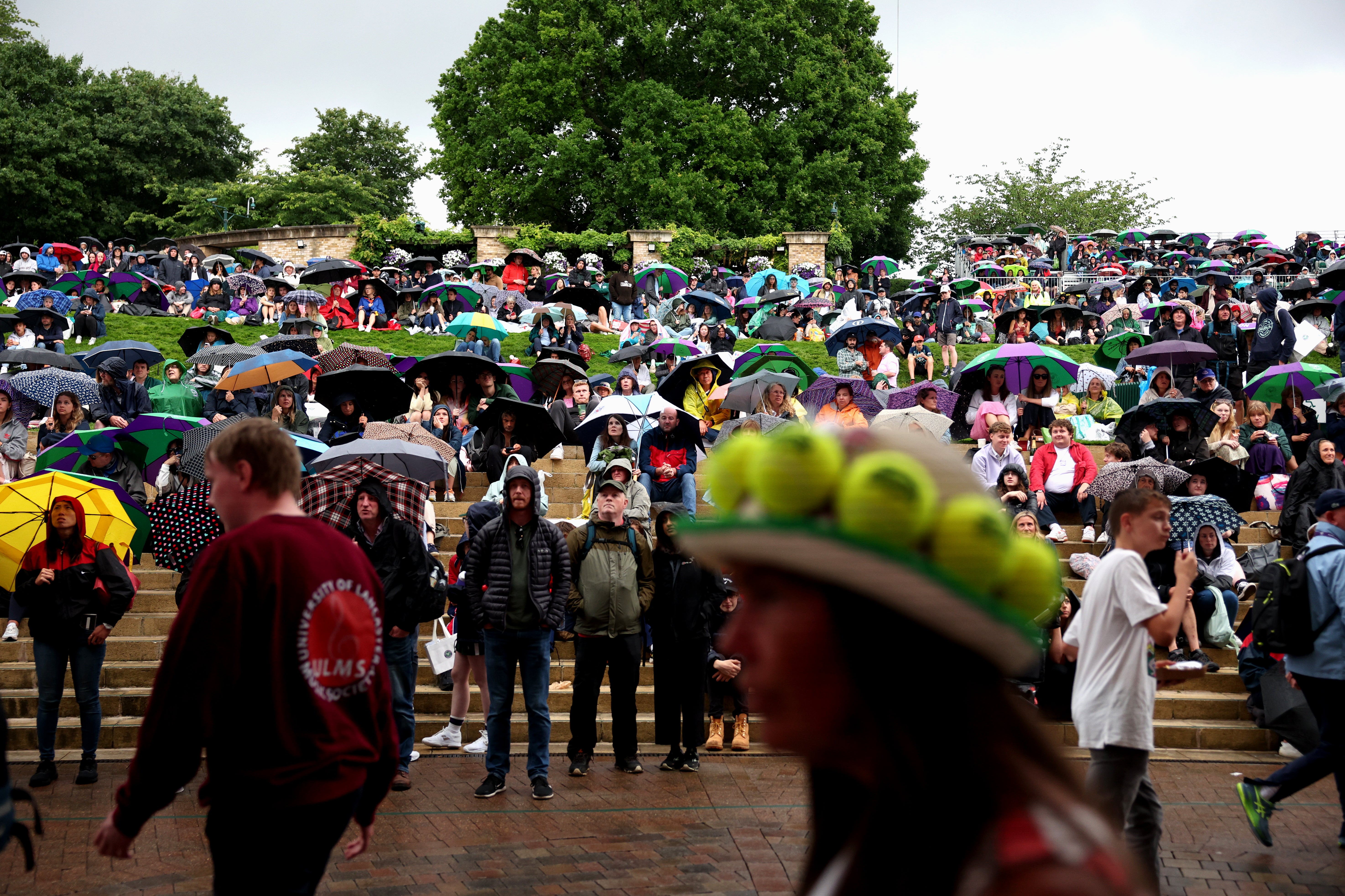 Spectators shelter from the rain with umbrellas and watch the Centre Court and Court 1 matches on the hill during day two of The Championships Wimbledon 2023 at All England Lawn Tennis and Croquet Club