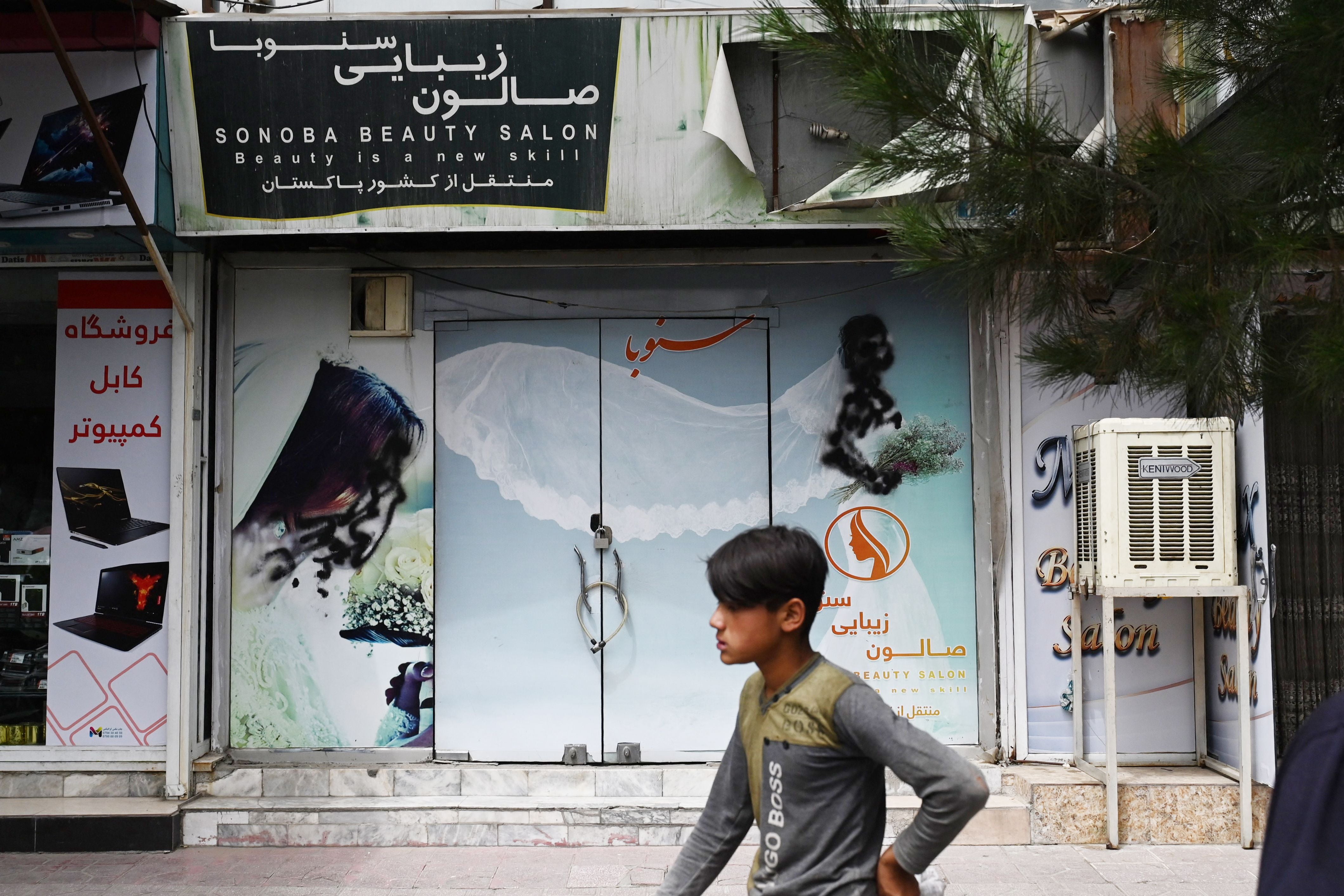 A youth walks past a closed beauty salon with images of women defaced at Shahr-e Naw area in Kabul