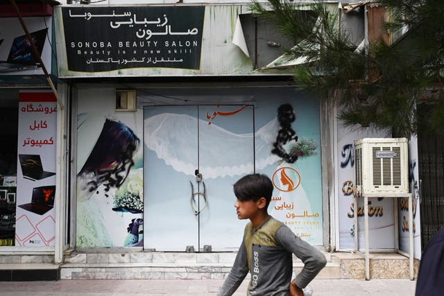 <p>A youth walks past a closed beauty salon with images of women defaced at Shahr-e Naw area in Kabul</p>