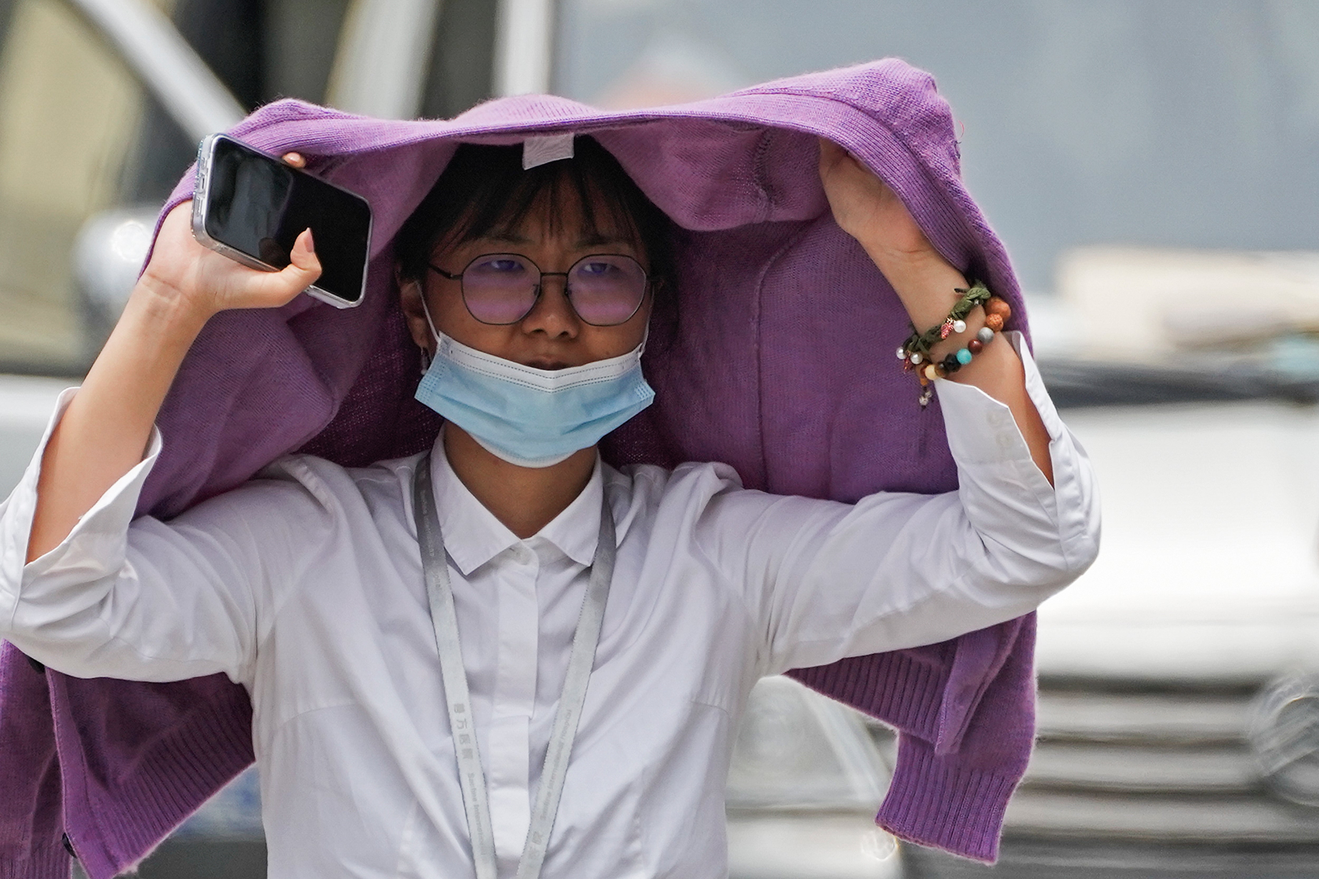 <p>A woman uses a sweater to shield from the sun as she walls on a street on a hot day in Beijing</p>