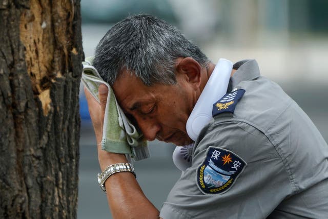 <p>A security guard wearing an electric fan on his neck wipes his sweat on a hot day in Beijing</p>