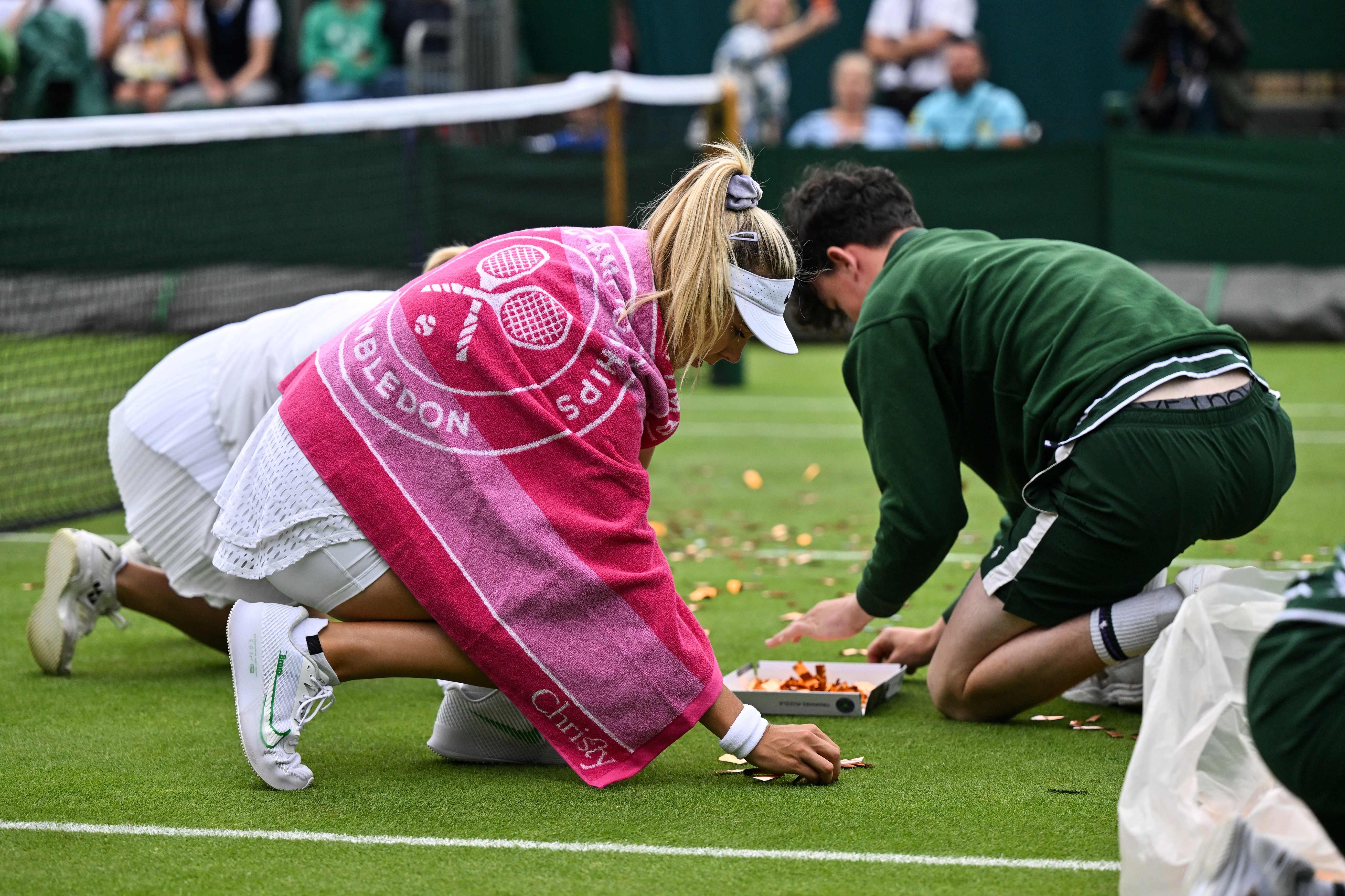 Katie Boulter helps ball boys and girls to pick up orange confetti after the disruption