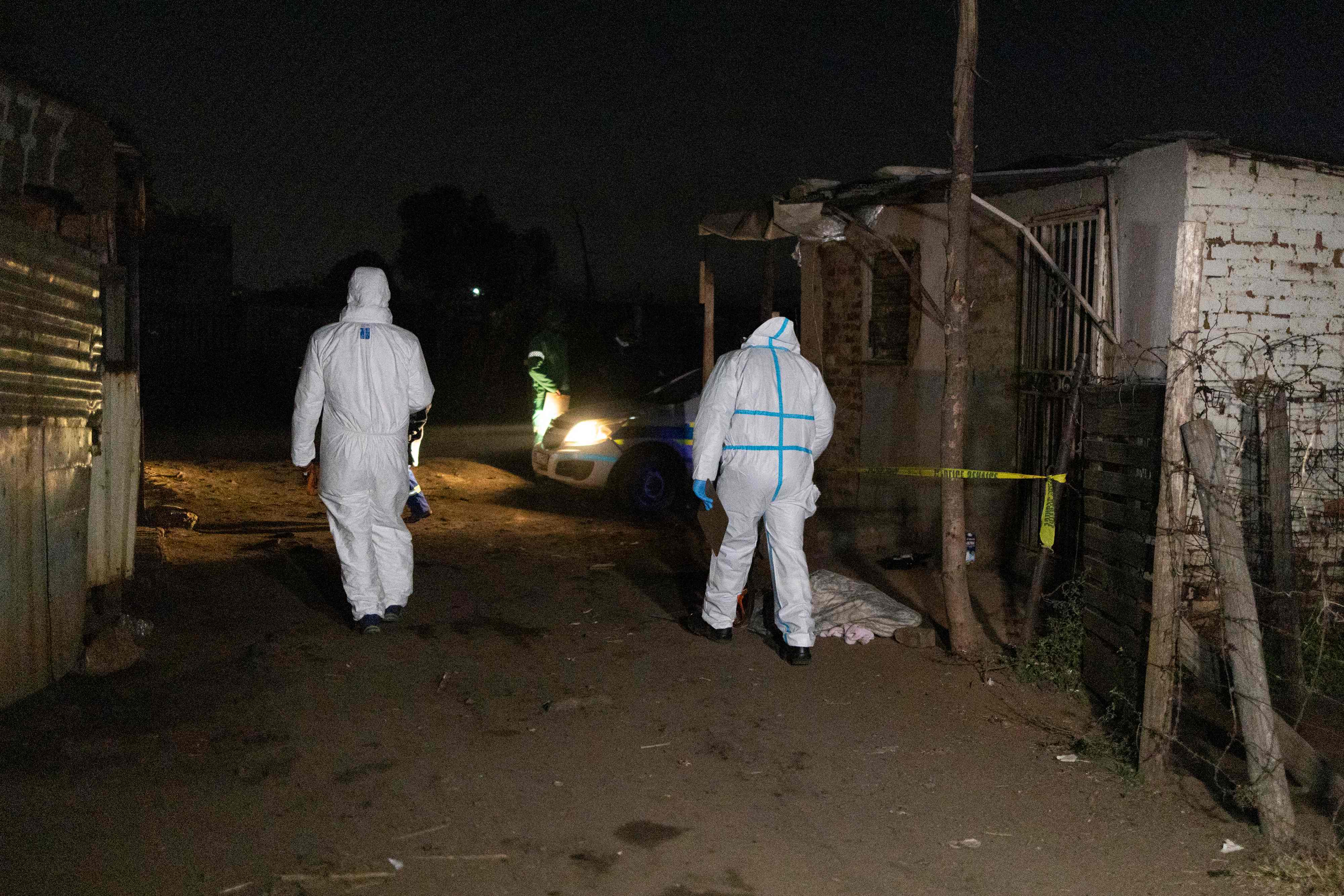 Members of the South African Police Service’s (SAPS) forensic department walk past a body covered with a blanket