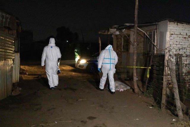 <p>Members of the South African Police Service’s (SAPS) forensic department walk past a body covered with a blanket </p>